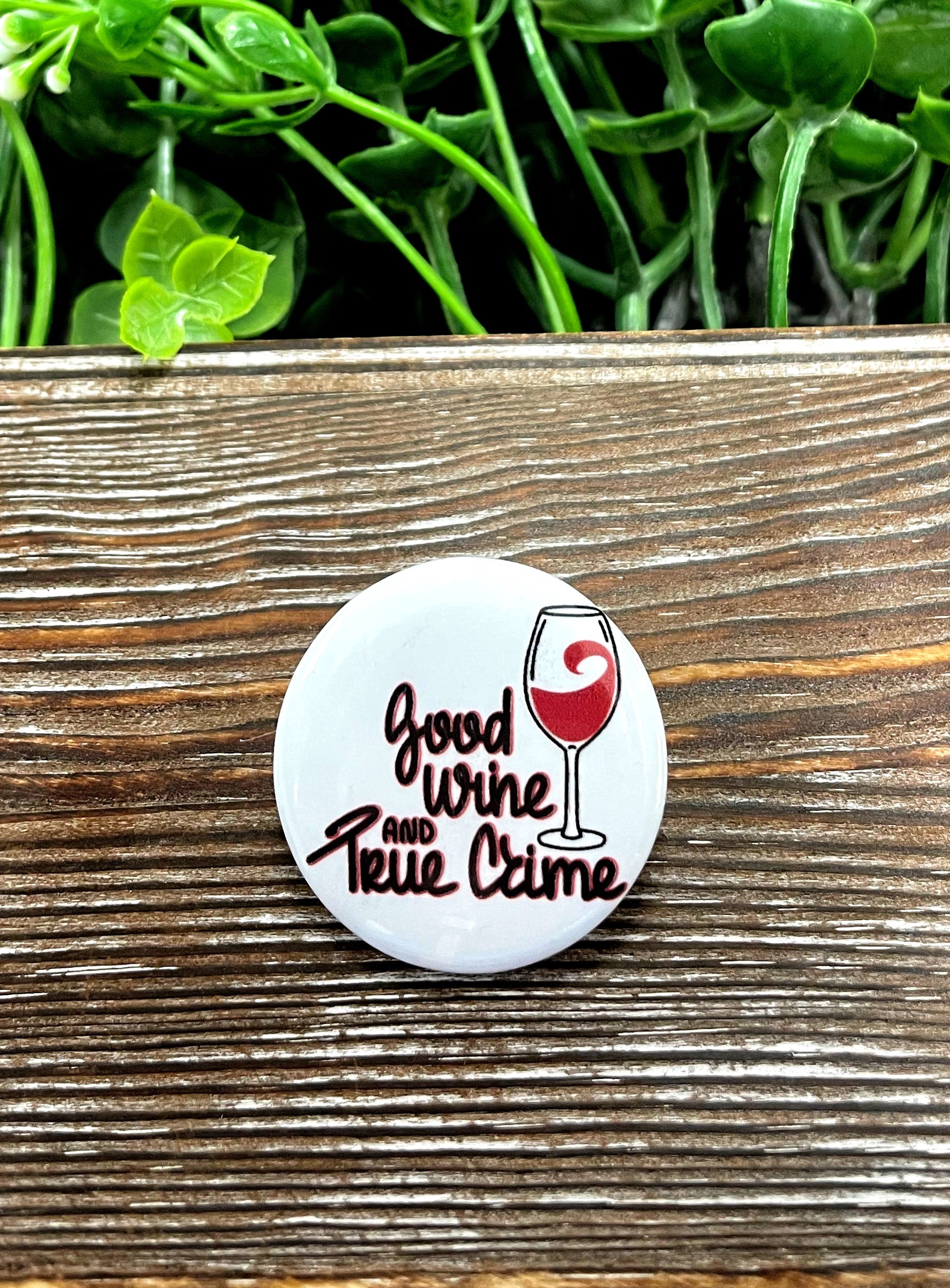 A stylish 1.25-inch button featuring a graphic design that combines elements of wine and true crime, perfect for personal expression.