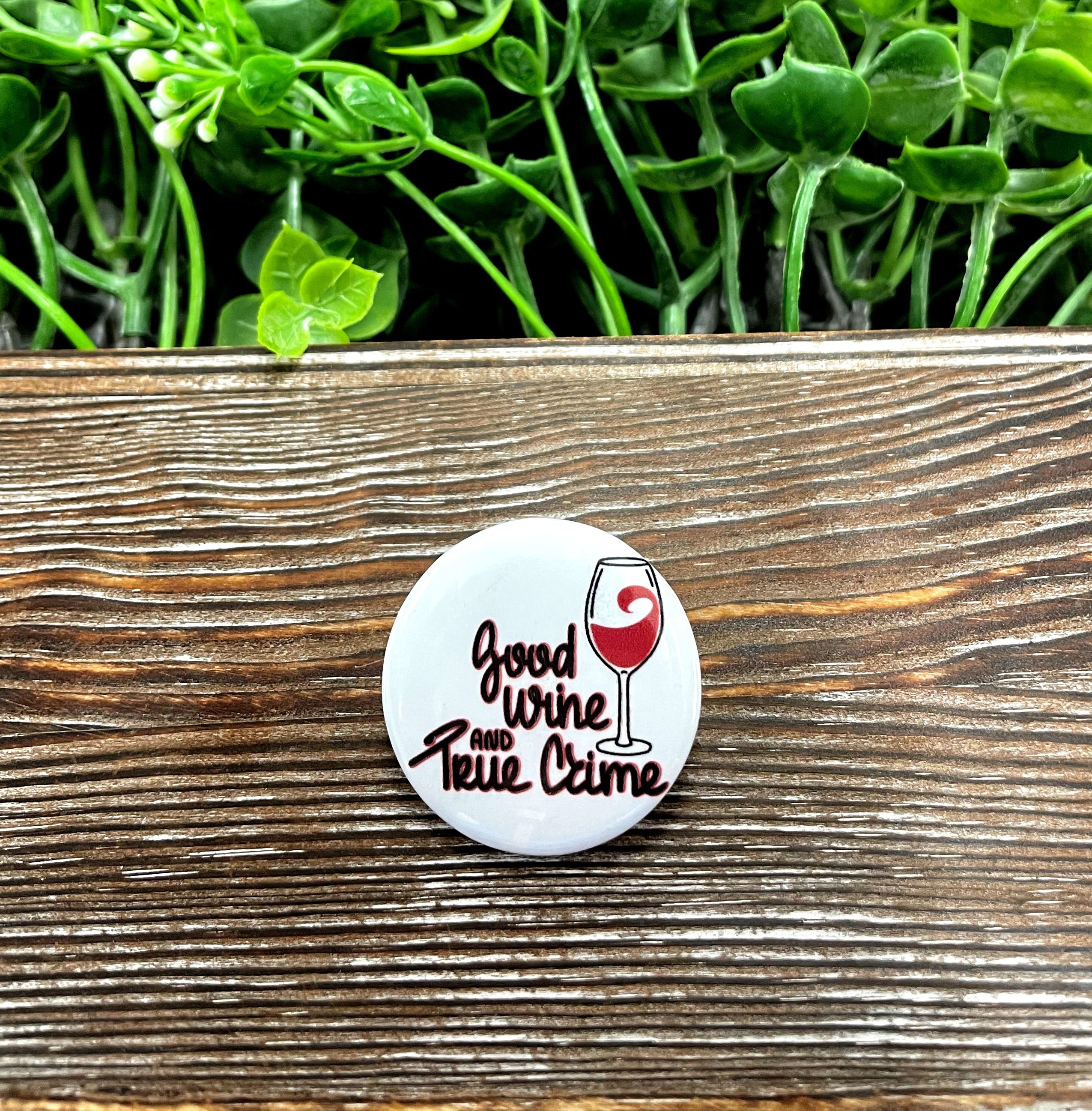 A stylish 1.25-inch button featuring a graphic design that combines elements of wine and true crime, perfect for personal expression.