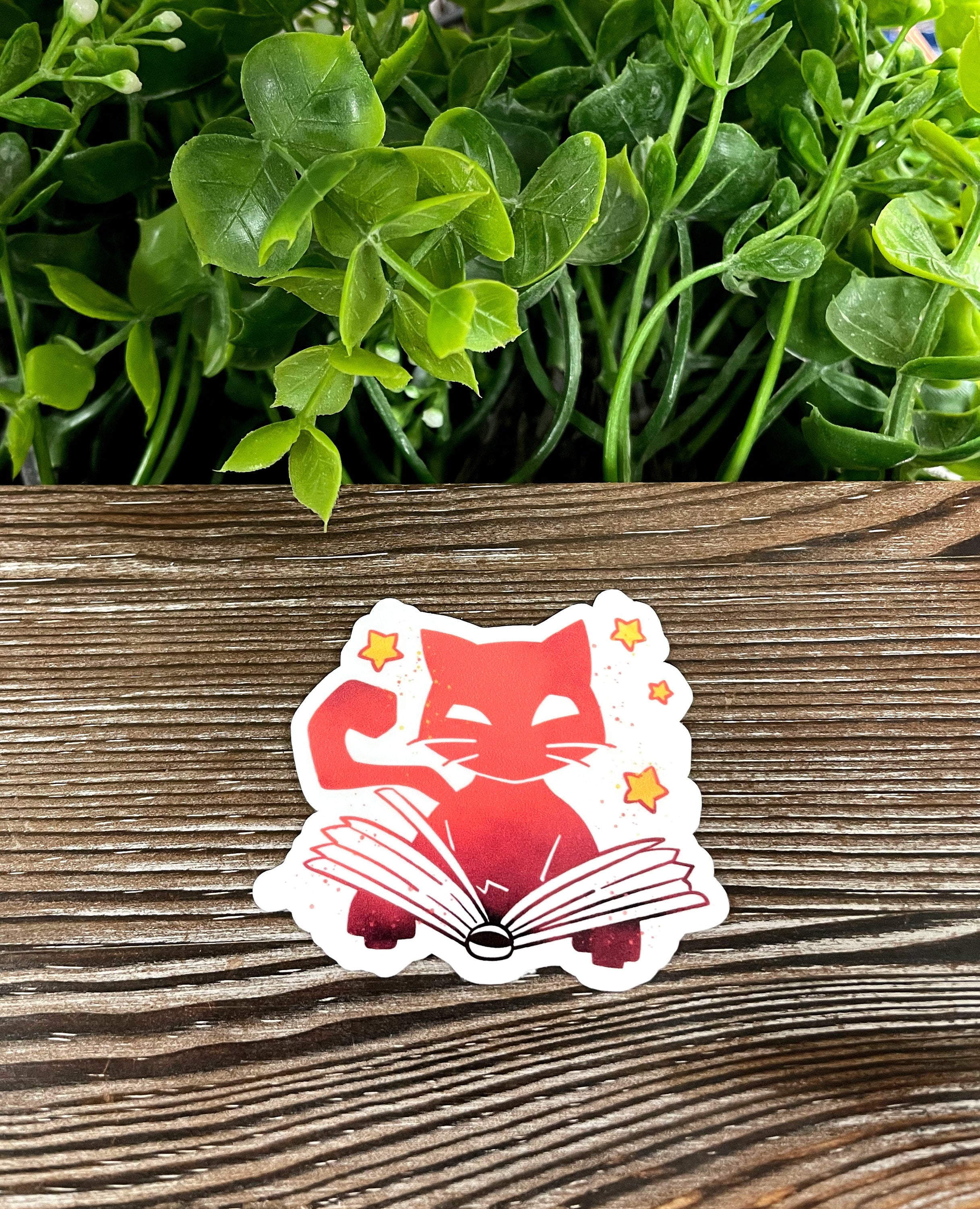 A vibrant die cut vinyl sticker featuring an orange cat reading a book, perfect for Halloween decoration.