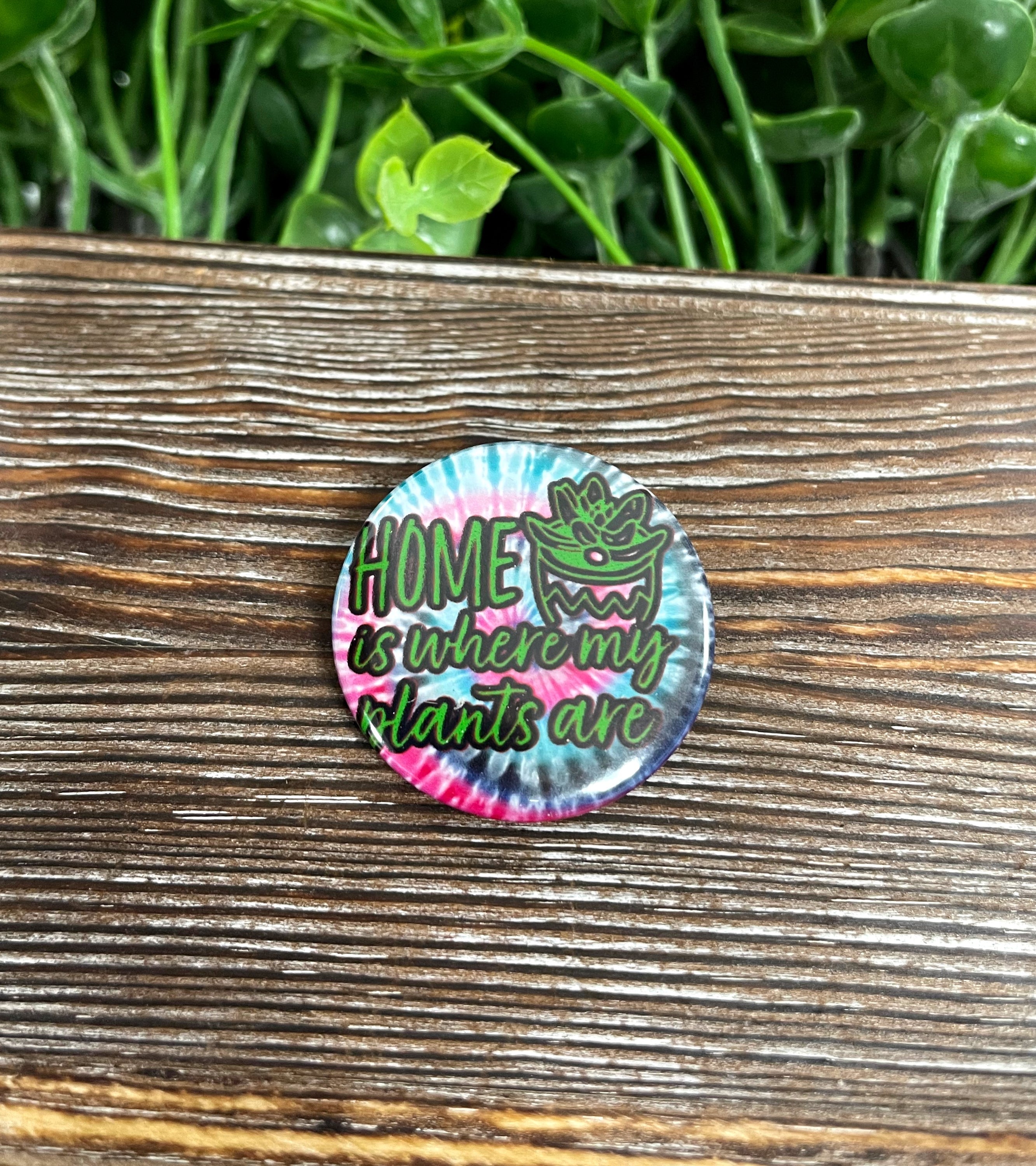 A vibrant 1.25-inch graphic art button featuring a red and blue design with the phrase 'Home is Where my Plants Are'.