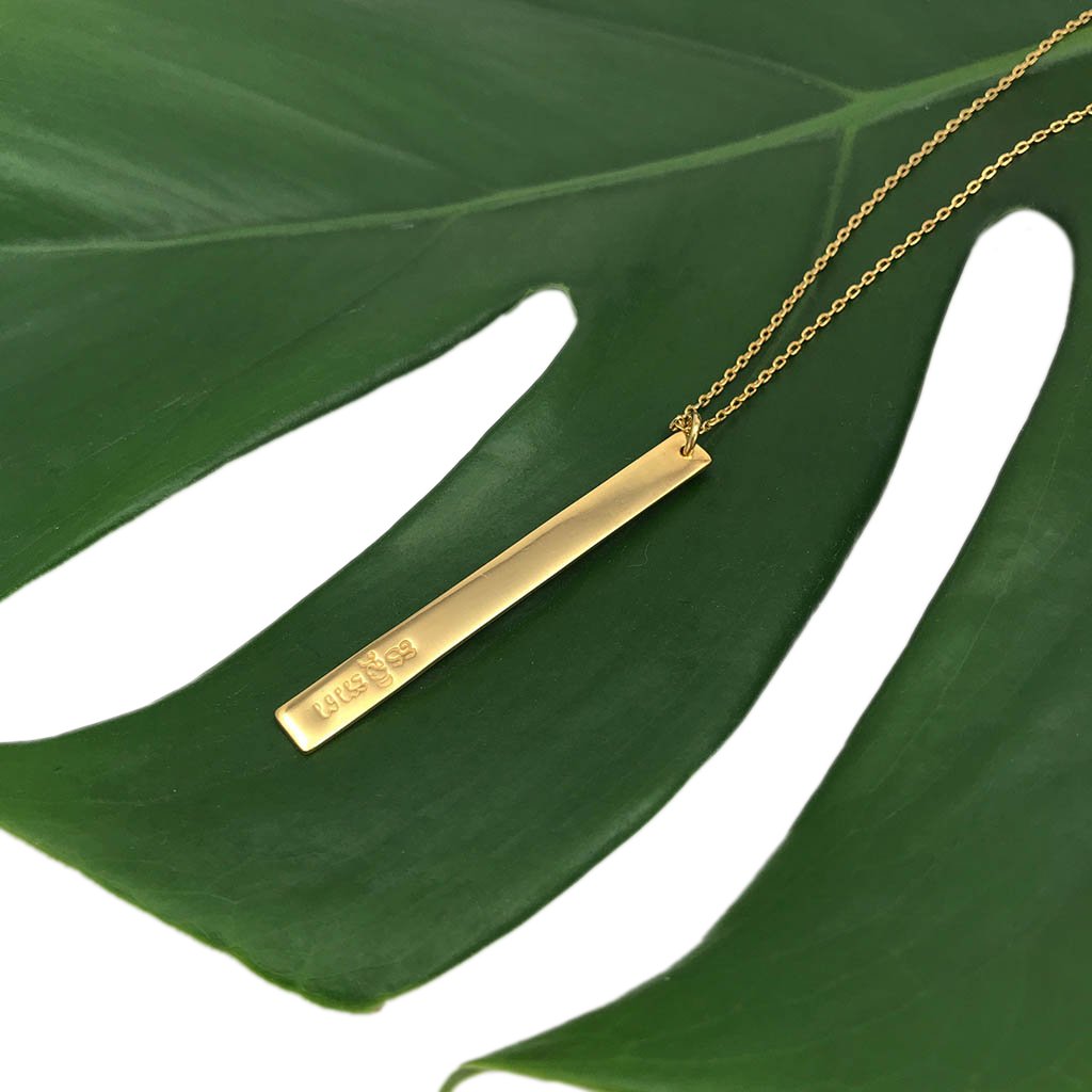 Layered Bar Bullet Necklace featuring recycled brass and bullet fragments, with a bar inscribed with 'peace' in Khmer, showcasing its unique design.