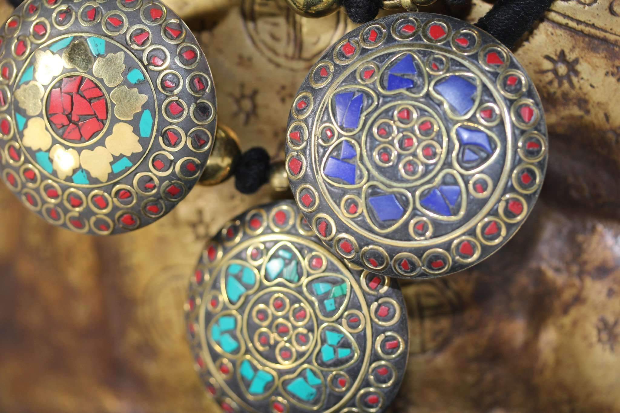 A vibrant Mosaic Medallion Necklace featuring colorful chips in a brass pendant, suspended on a black cotton chord with gold tone ball charms.