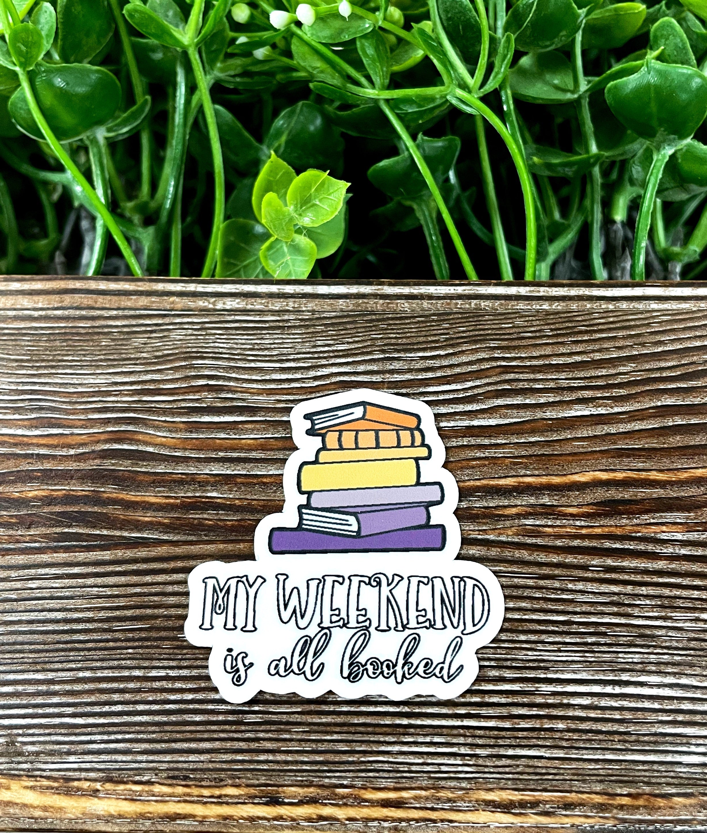 A colorful die cut sticker featuring the phrase 'My Weekend is Booked' with graphic book illustrations, perfect for personalizing items.