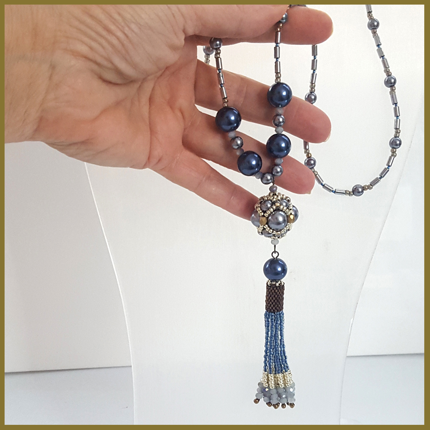 Hand holding beaded necklace with tassel.