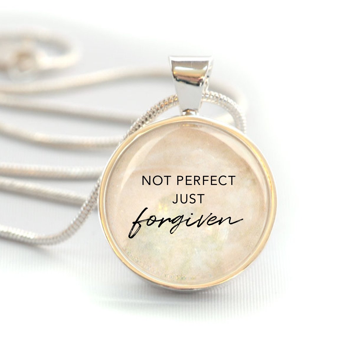 A silver-plated Christian pendant necklace featuring the words 'Not Perfect, Just Forgiven' under a glass cabochon, strung on a 20-inch chain.