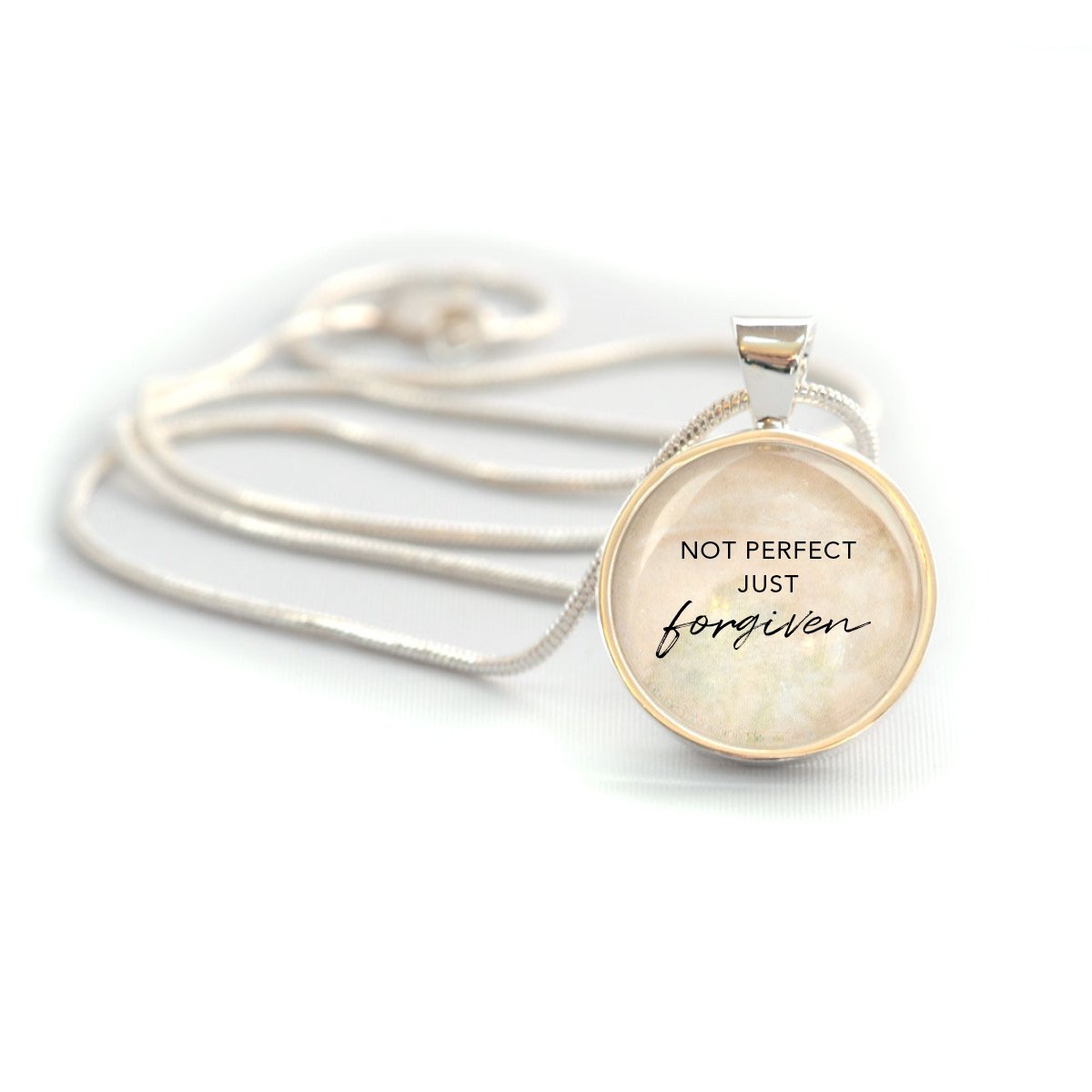 A silver-plated Christian pendant necklace featuring the words 'Not Perfect, Just Forgiven' under a glass cabochon, strung on a 20-inch chain.