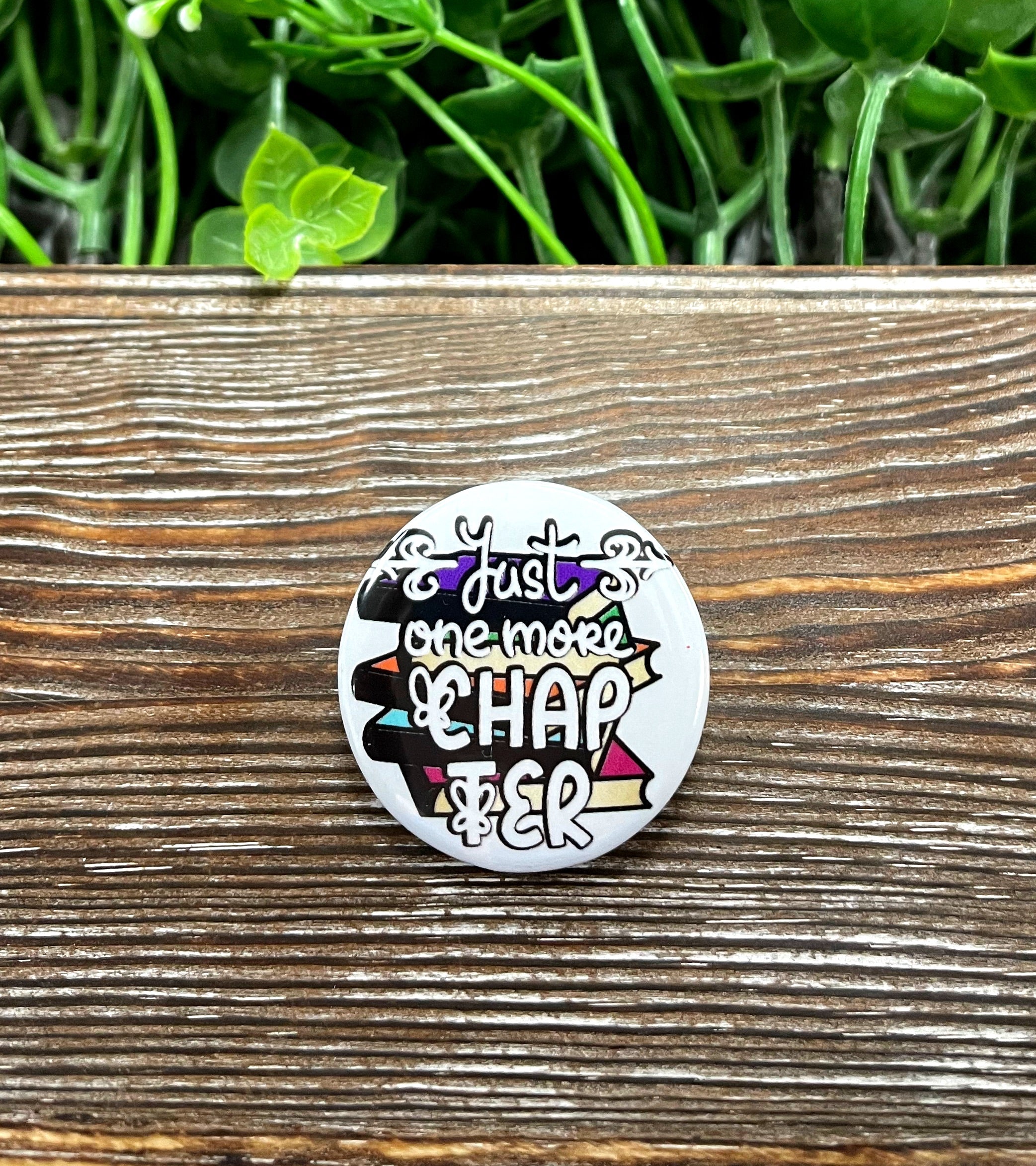 A 1.25-inch button featuring a stack of books with the phrase 'One More Chapter', perfect for book lovers.