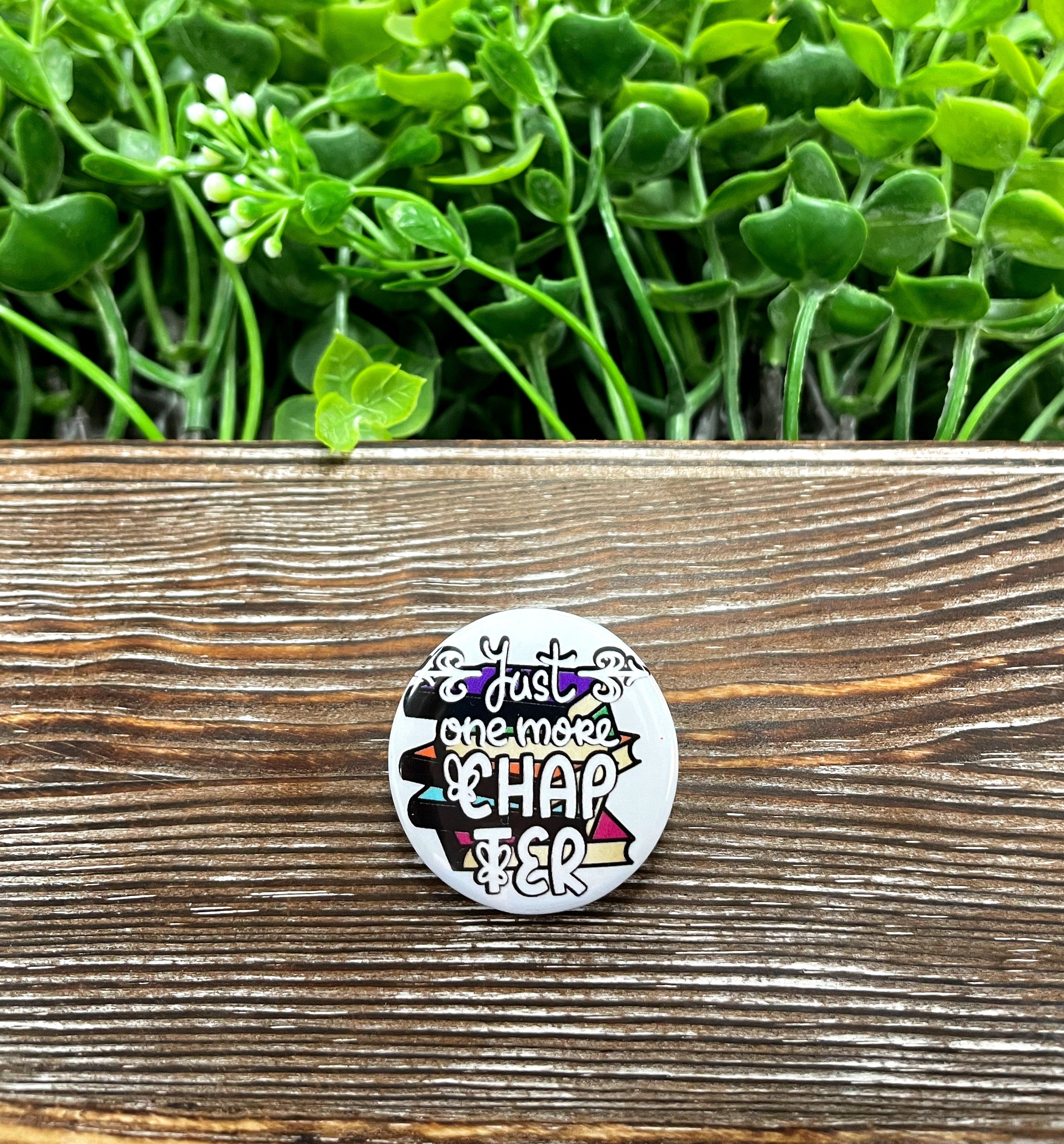 A 1.25-inch button featuring a stack of books with the phrase 'One More Chapter', perfect for book lovers.