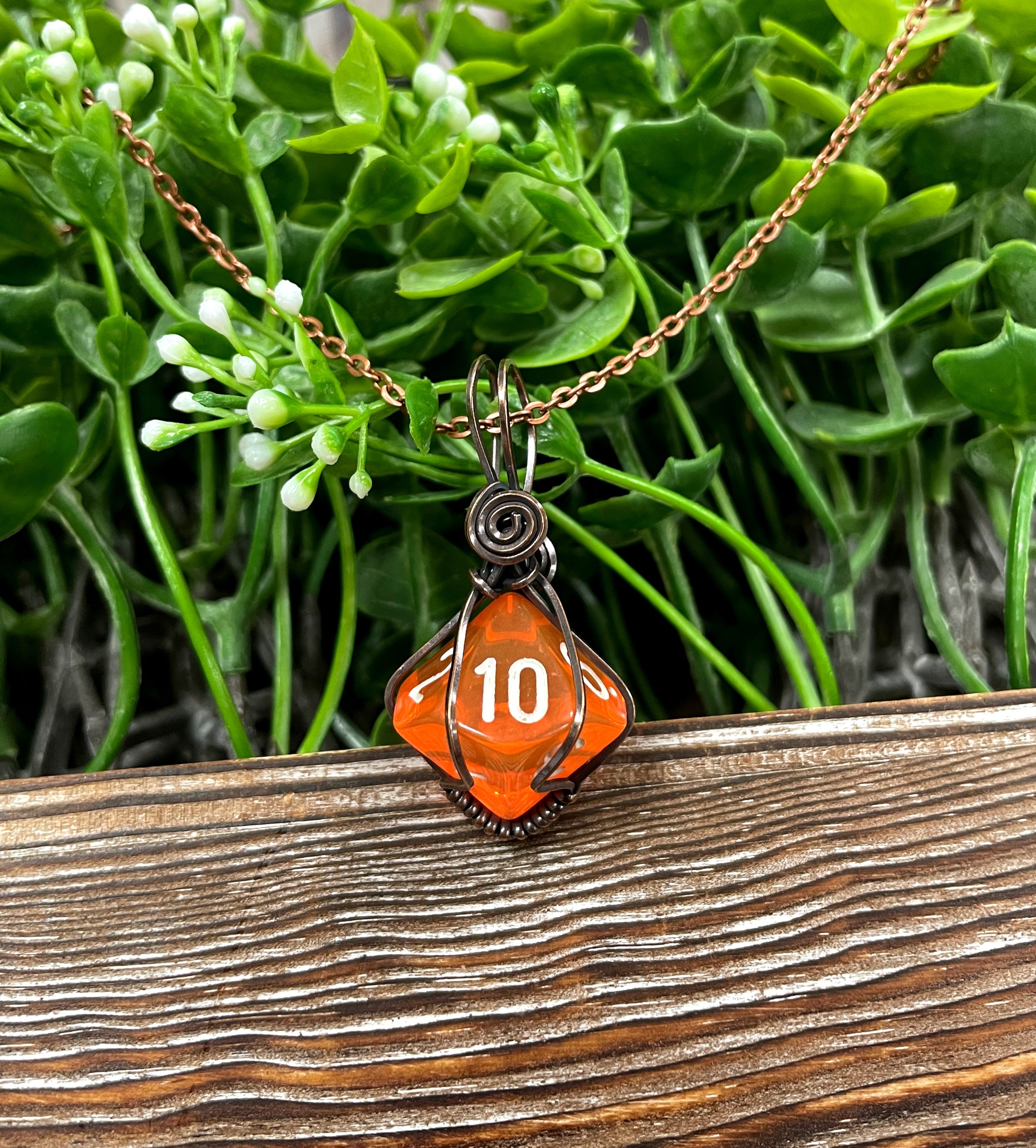 Orange D10 gamer dice wrapped in oxidized copper wire, hanging from a 21-inch suede leather cord, showcasing a unique and antique look.