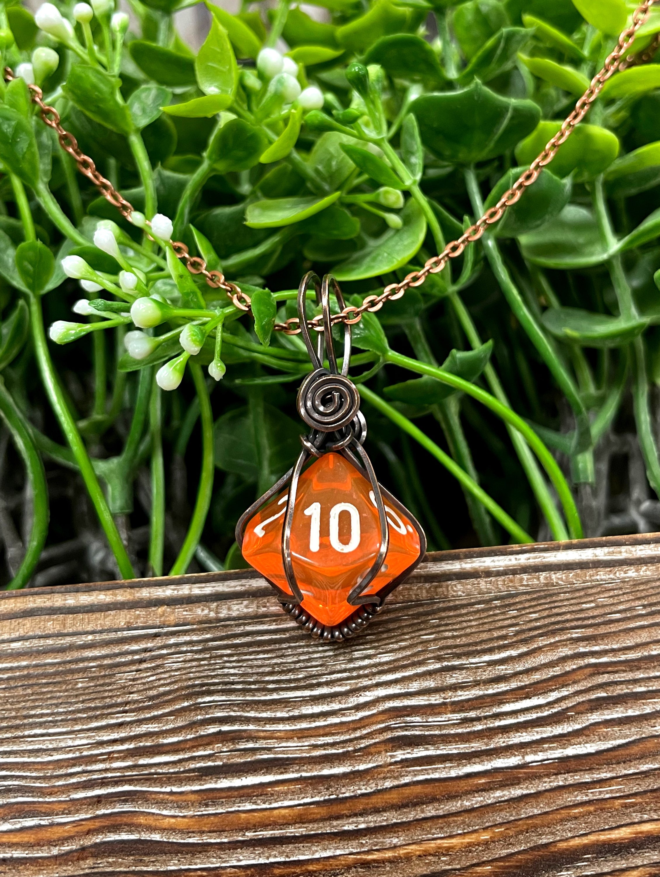 Orange D10 gamer dice wrapped in oxidized copper wire, hanging from a 21-inch suede leather cord, showcasing a unique and antique look.