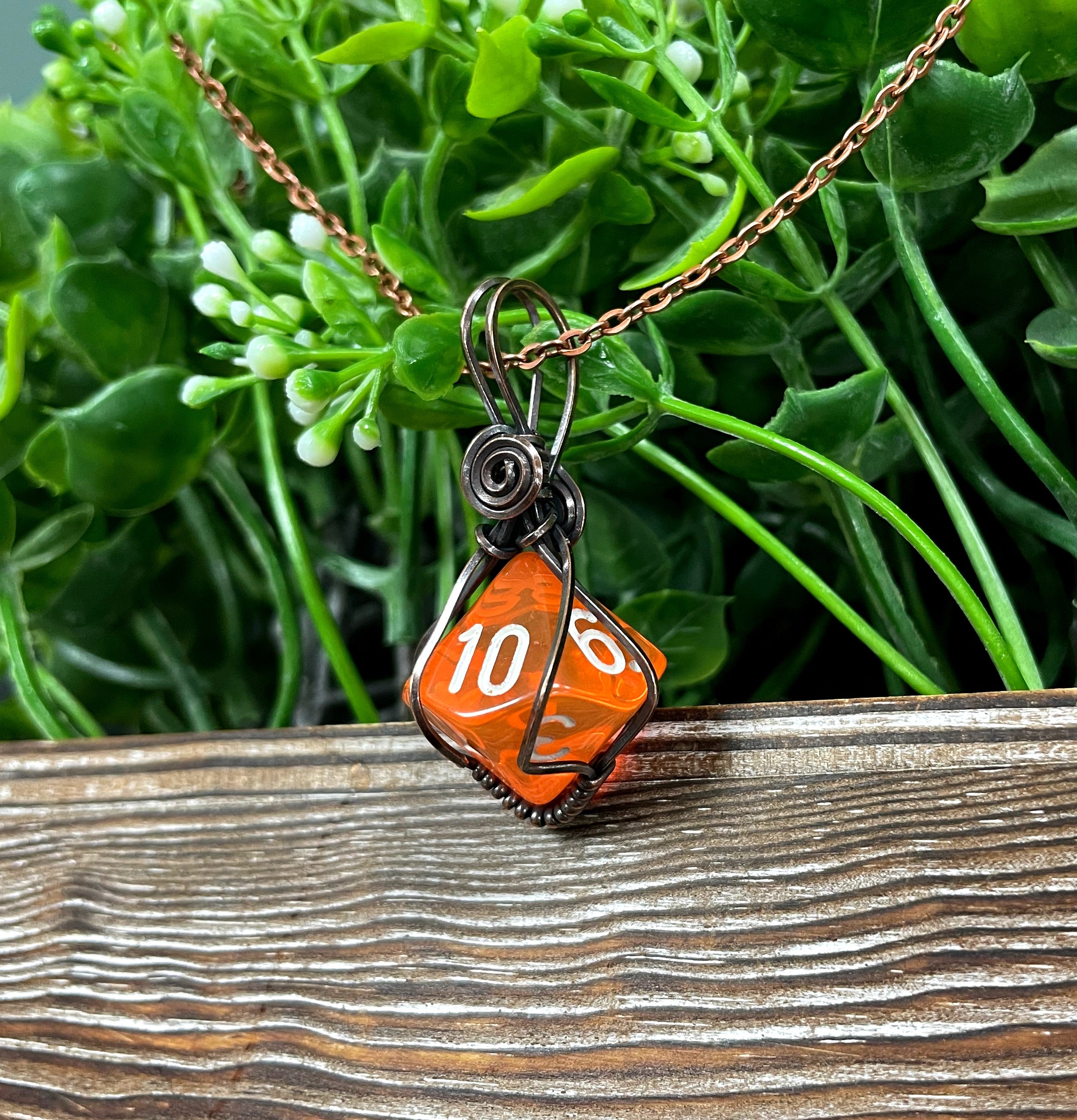 Orange D10 gamer dice wrapped in oxidized copper wire, hanging from a 21-inch suede leather cord, showcasing a unique and antique look.