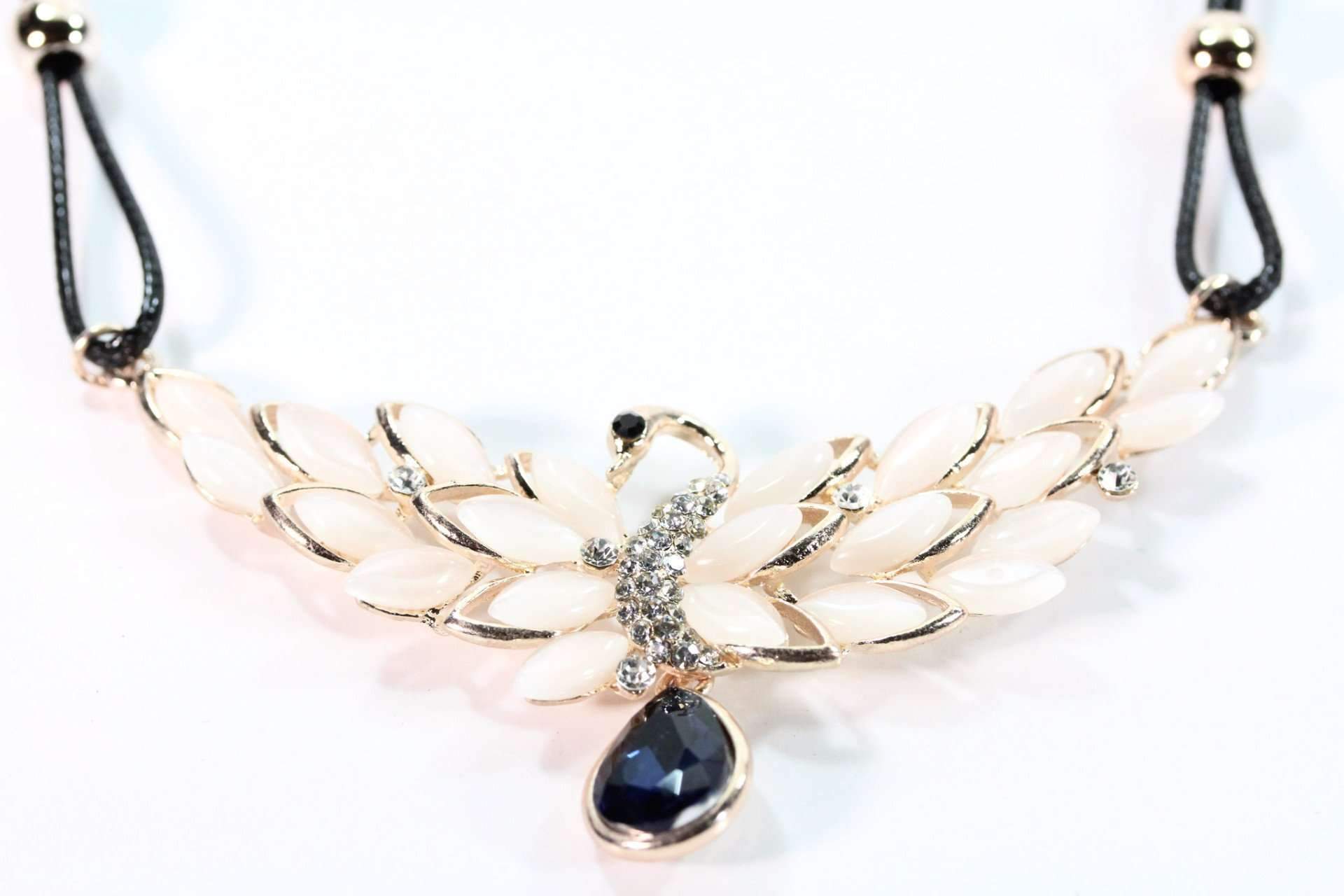 A stunning Peacock Pendant Necklace featuring sparkling white crystals, royal blue diamond accent, and peach marquise cut faux stones on a black chord.