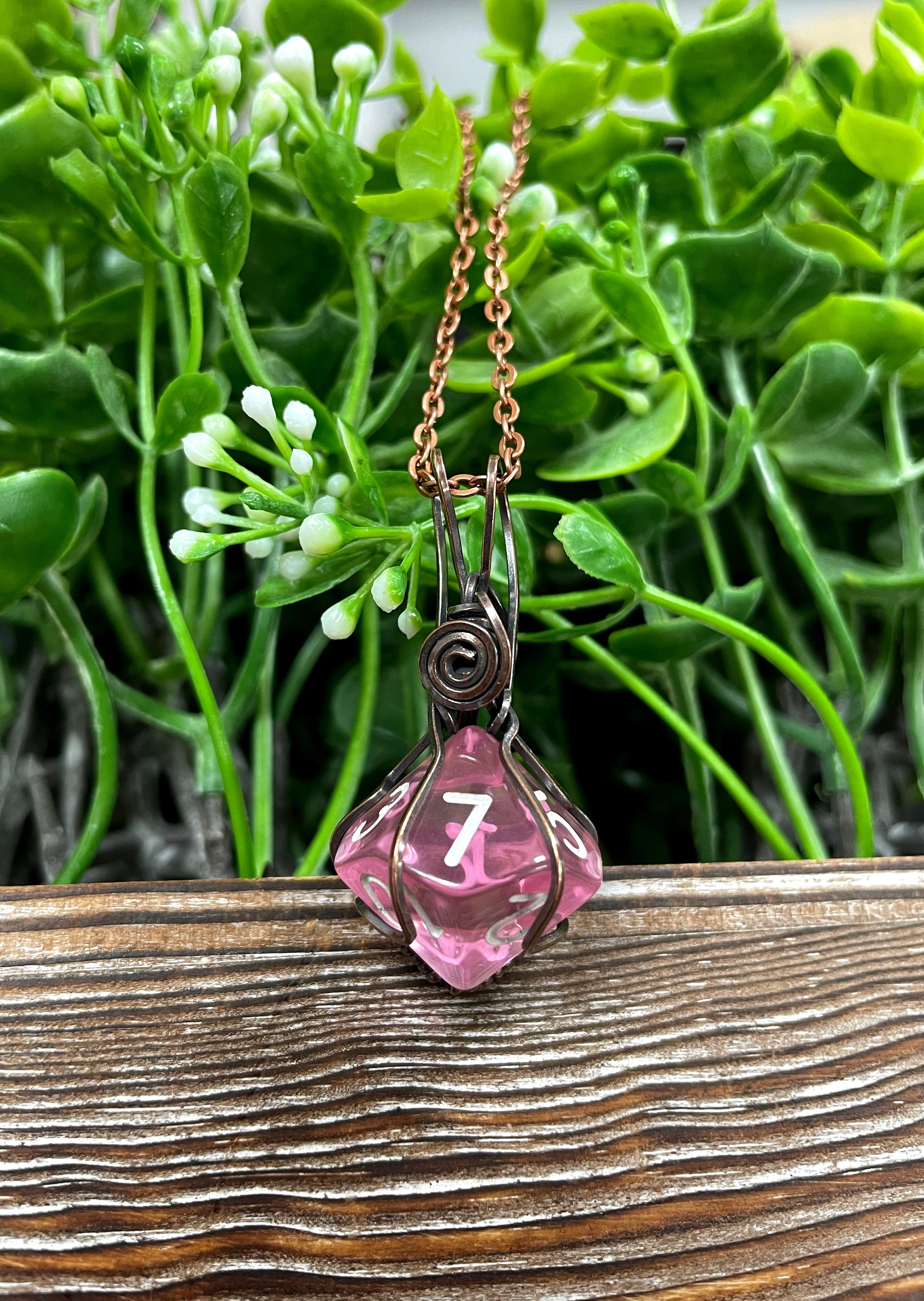 A beautiful pink D10 dice pendant wrapped in oxidized copper wire, hanging from a 21-inch suede leather cord, showcasing its unique design.