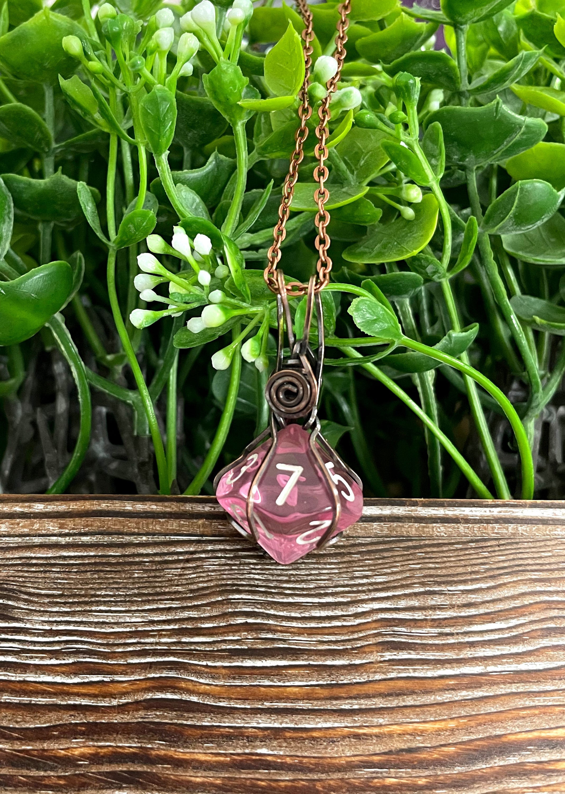 A beautiful pink D10 dice pendant wrapped in oxidized copper wire, hanging from a 21-inch suede leather cord, showcasing its unique design.