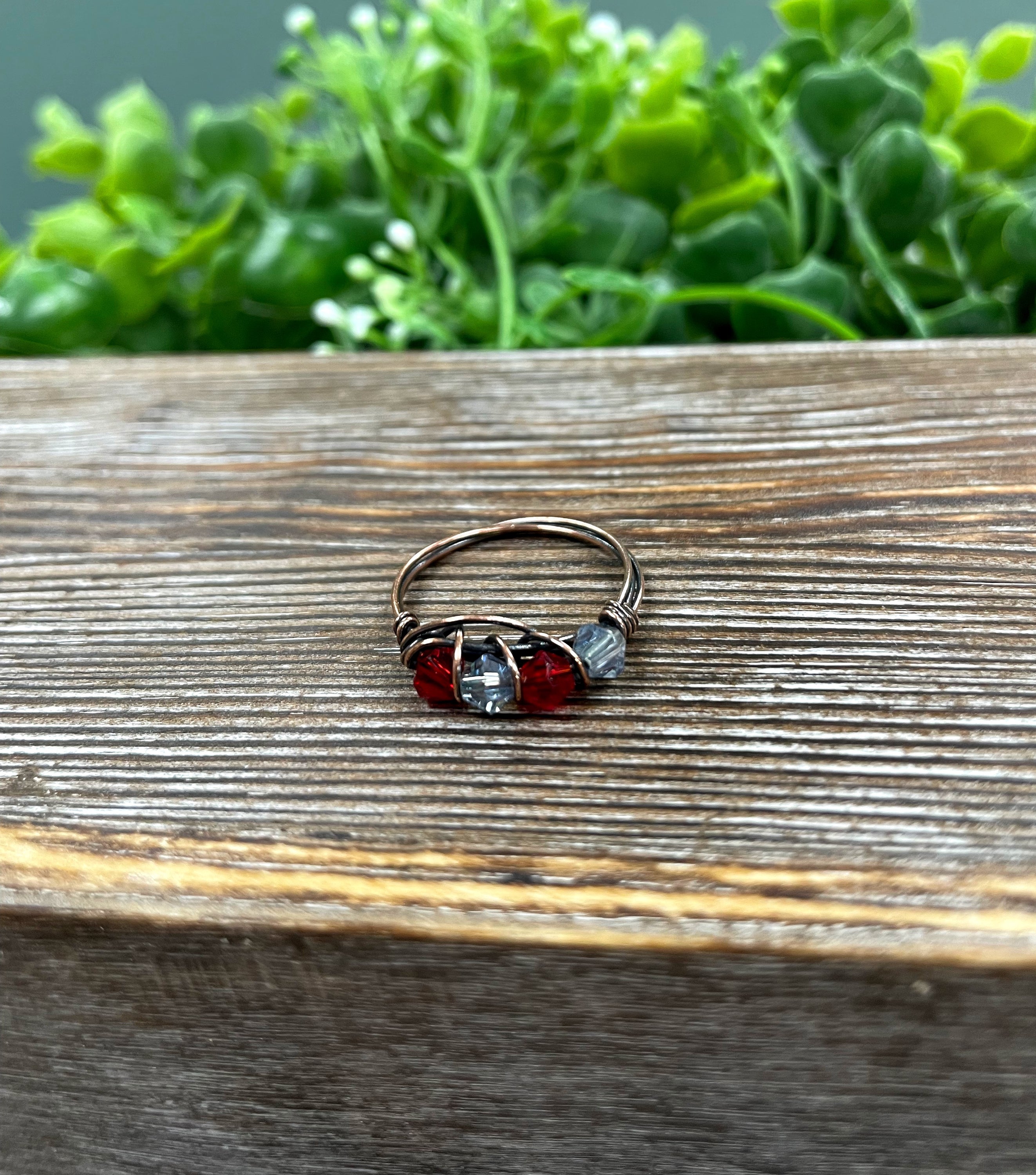 A beautifully handcrafted Red and Grey Glass Crystal Wire Wrapped Ring featuring vibrant glass beads wrapped in oxidized copper wire.