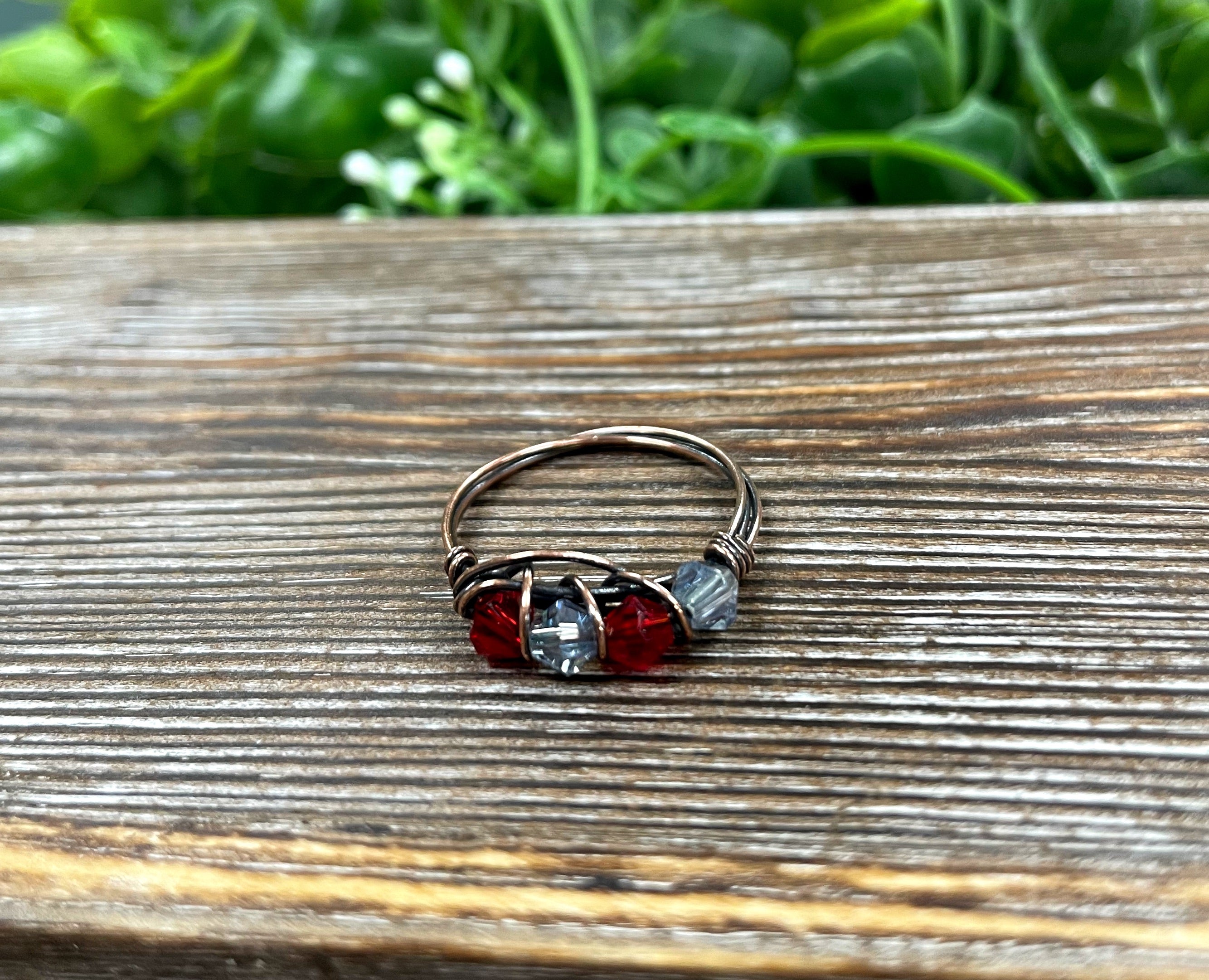 A beautifully handcrafted Red and Grey Glass Crystal Wire Wrapped Ring featuring vibrant glass beads wrapped in oxidized copper wire.