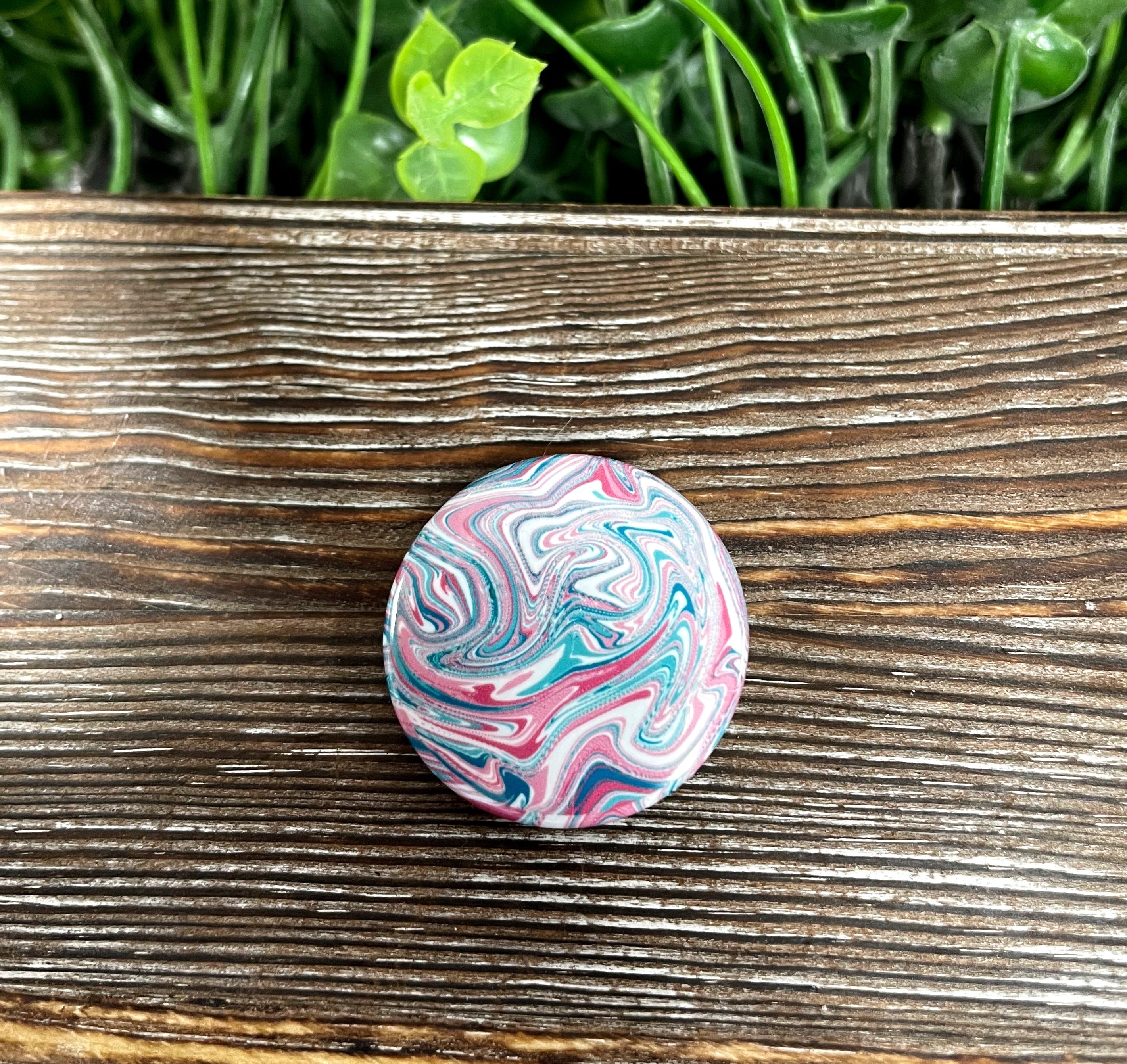 A vibrant 1.25-inch button featuring a red, blue, and white swirl design, perfect for personalizing bags and accessories.