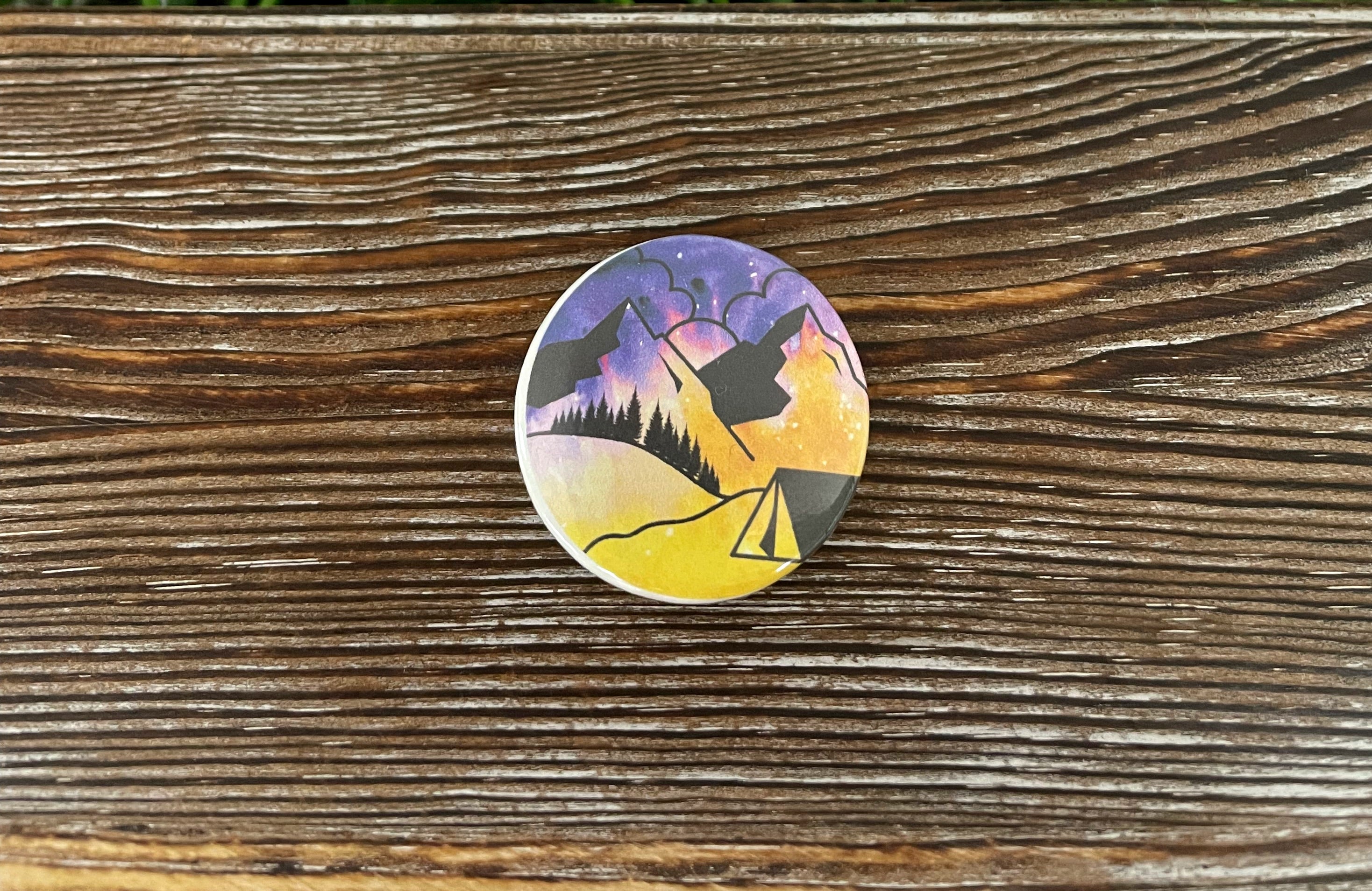 A colorful 1.25-inch button featuring a scenic mountain view design, perfect for personalizing bags and accessories.