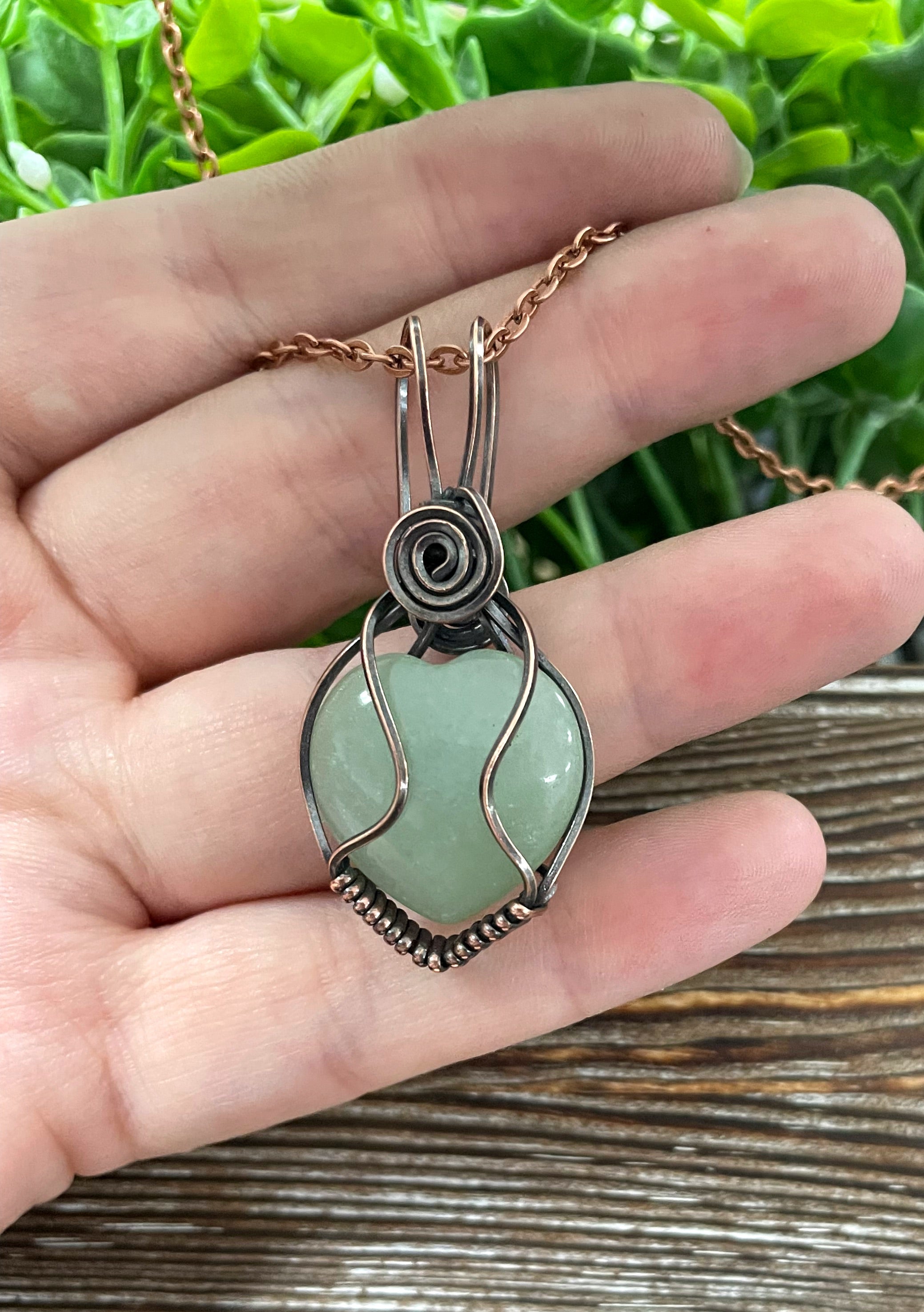 Small heart-shaped green aventurine gemstone pendant wrapped in oxidized copper wire, displayed on a 21-inch cord.