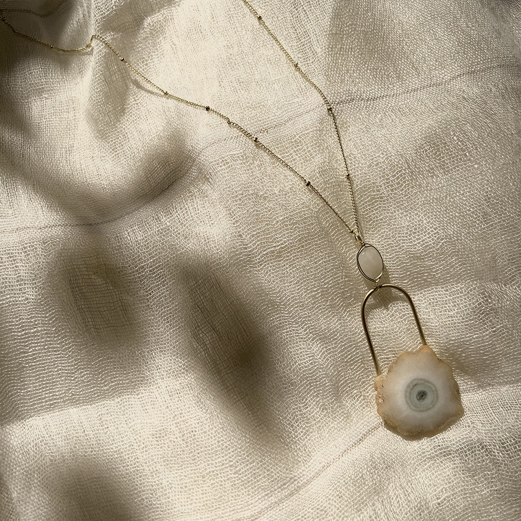 A beautifully crafted Solar Quartz Eye Necklace featuring a polished solar quartz stone and moon stone on a brass chain, showcasing unique colors and patterns.