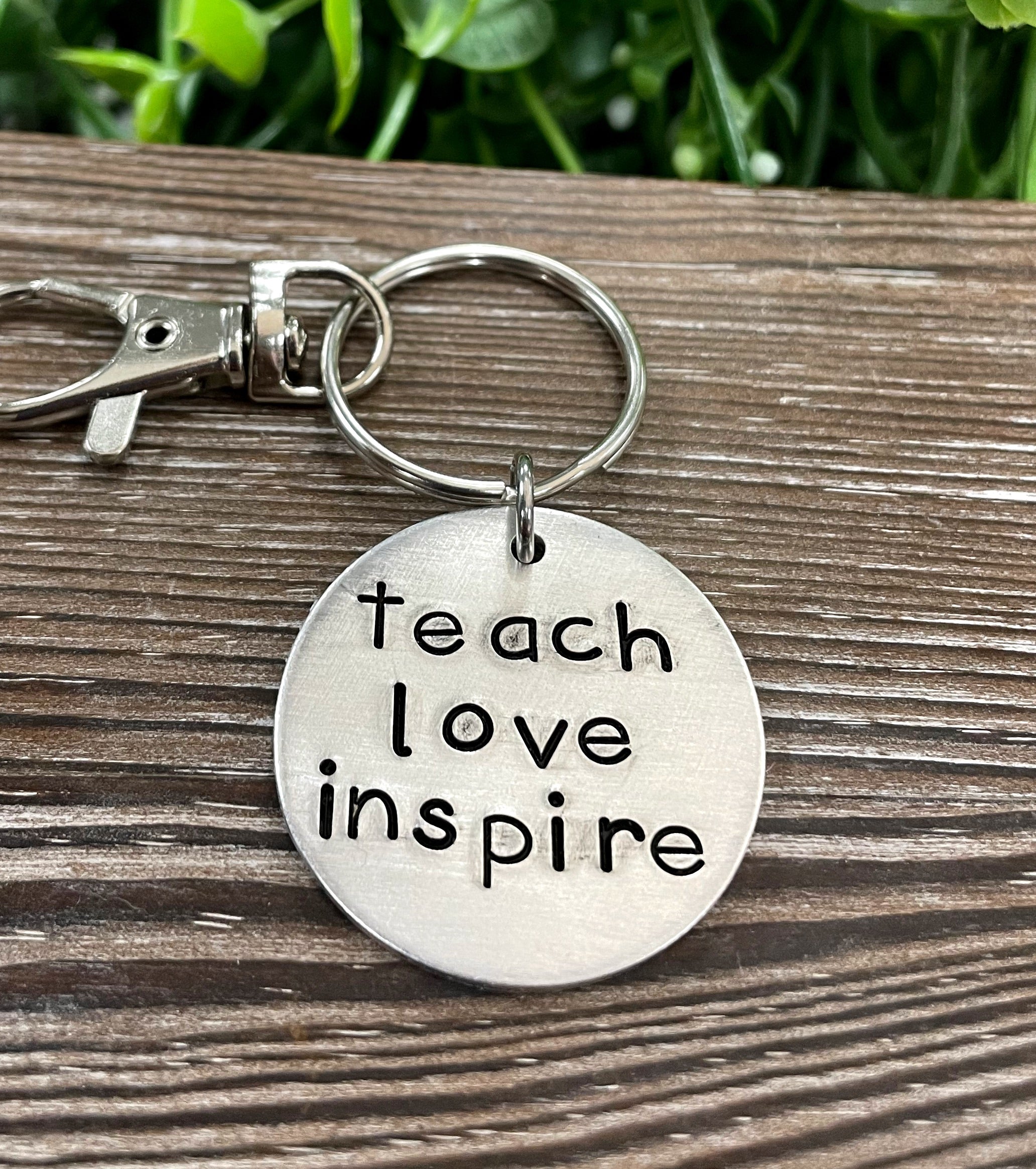 A hand stamped keychain featuring the motivational phrase 'Teach Love Inspire', showcasing unique letter spacing and craftsmanship.