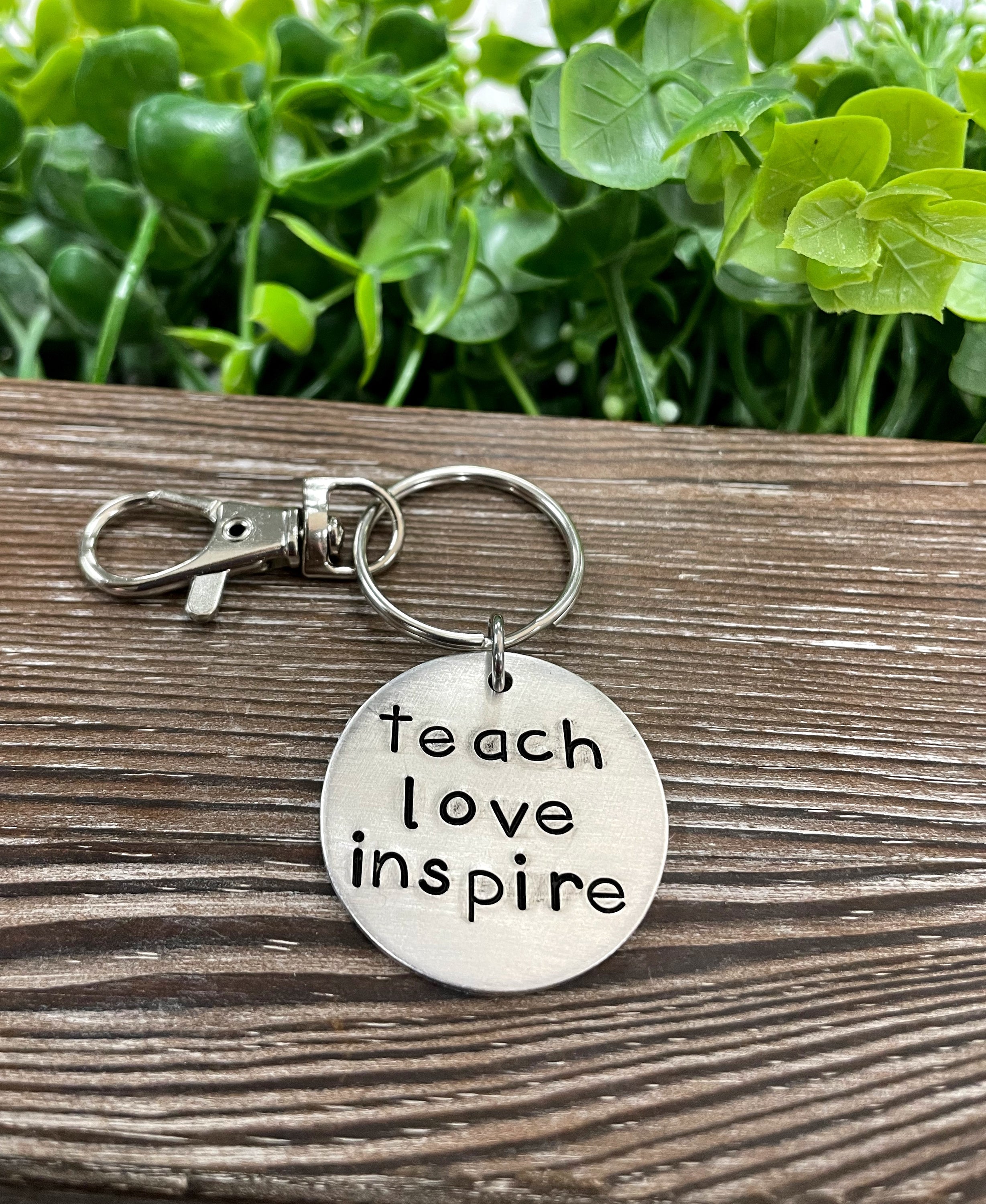 A hand stamped keychain featuring the motivational phrase 'Teach Love Inspire', showcasing unique letter spacing and craftsmanship.