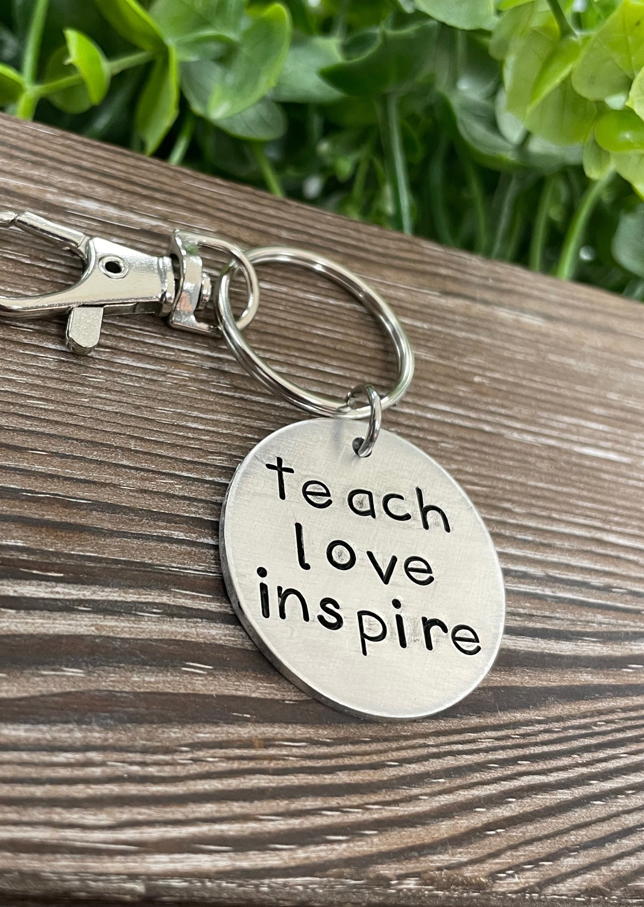 A hand stamped keychain featuring the motivational phrase 'Teach Love Inspire', showcasing unique letter spacing and craftsmanship.