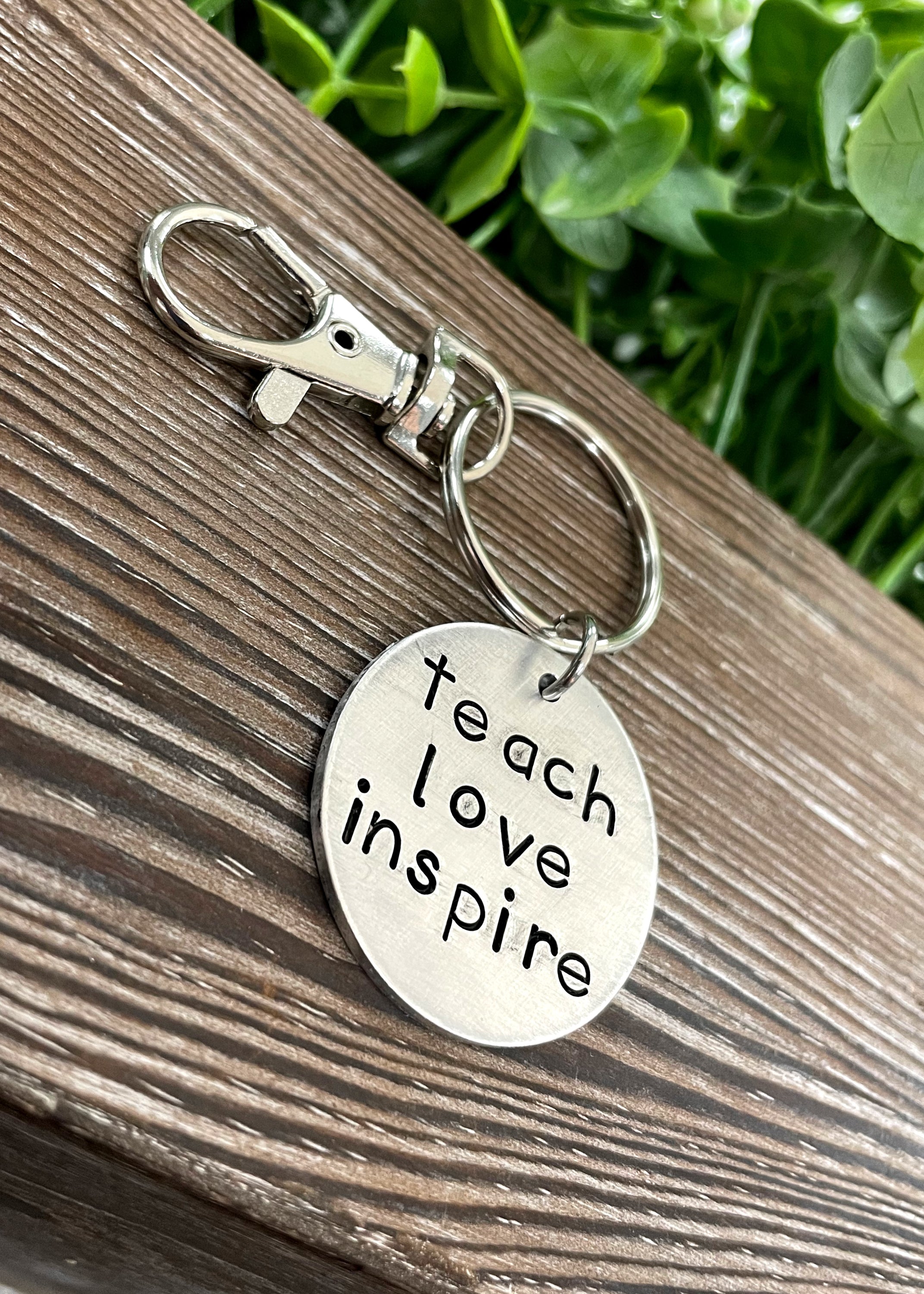 A hand stamped keychain featuring the motivational phrase 'Teach Love Inspire', showcasing unique letter spacing and craftsmanship.