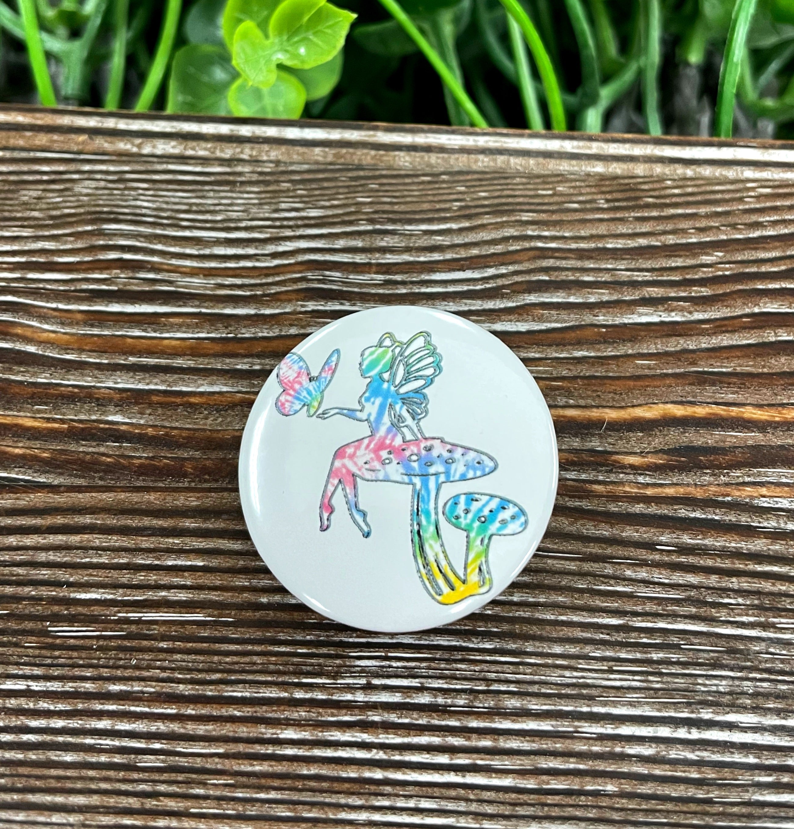 A colorful tie dye button featuring a whimsical fairy mushroom design, perfect for personalizing bags and accessories.