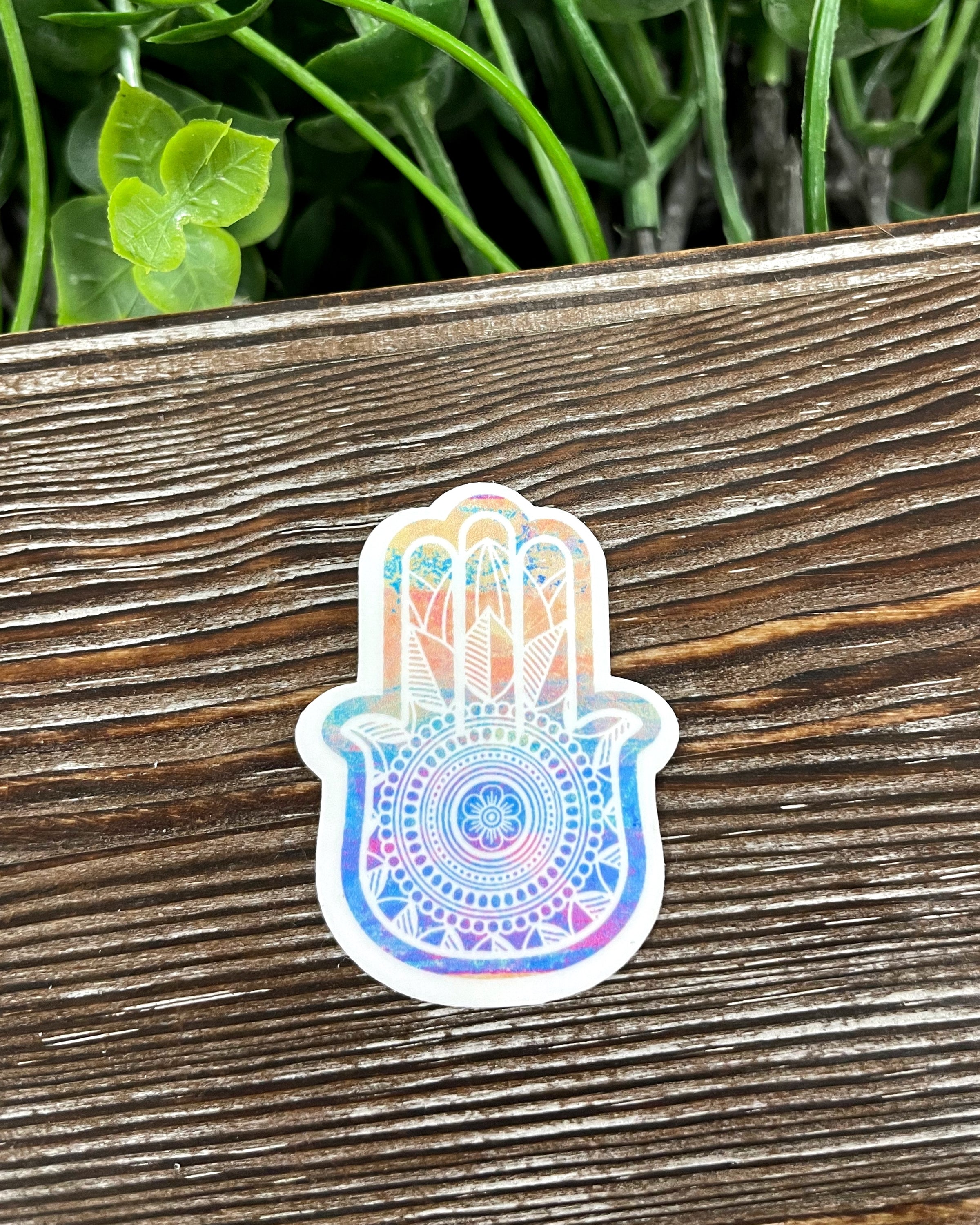 Colorful Tie Dye Hamsa Die Cut Sticker on a smooth surface, showcasing vibrant colors and intricate design.