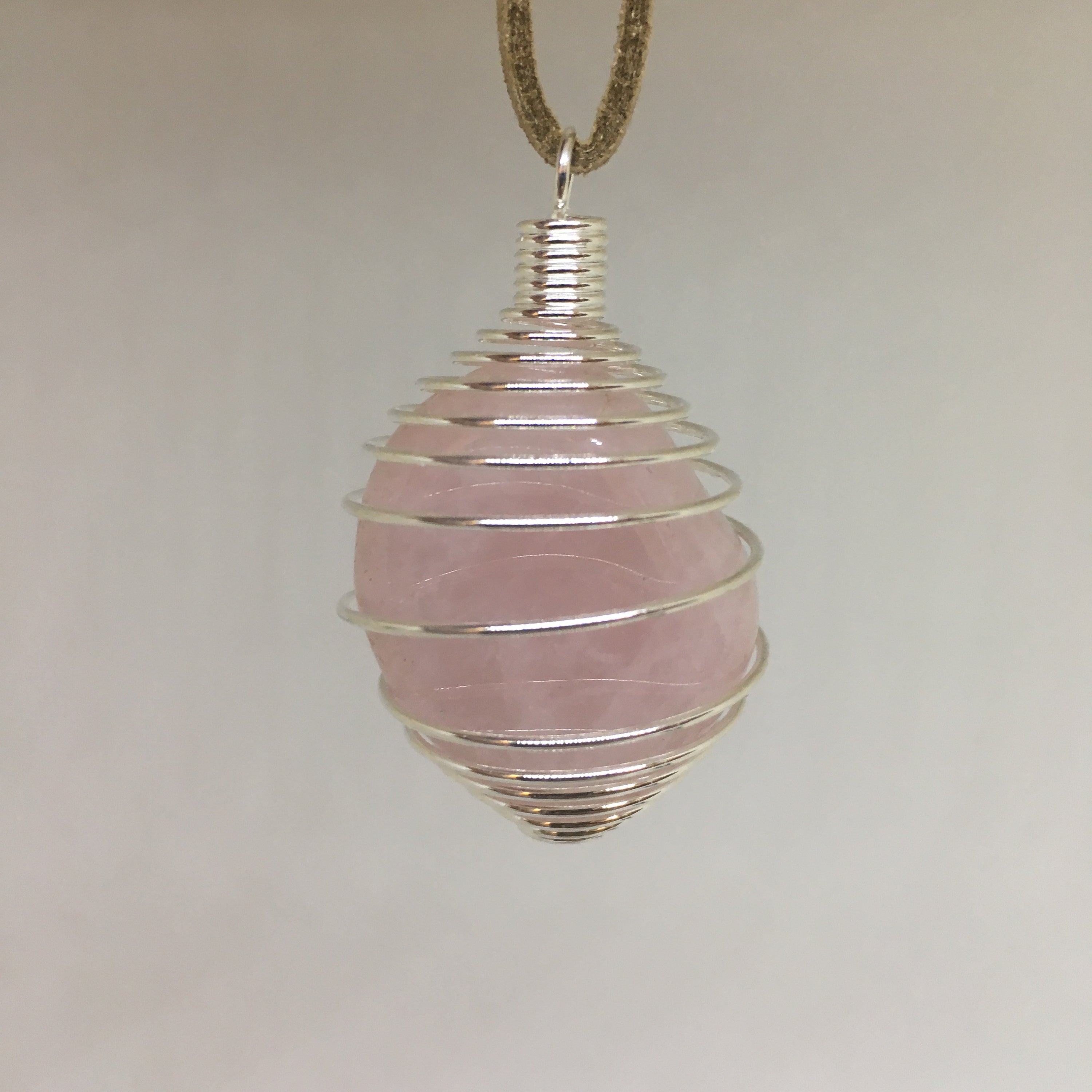 A collection of Tumbled Pendants featuring Opalite, Amethyst, Rose Quartz, Selenite, Angelite, and Hematite, elegantly displayed with a silver cage and tan suede necklace.