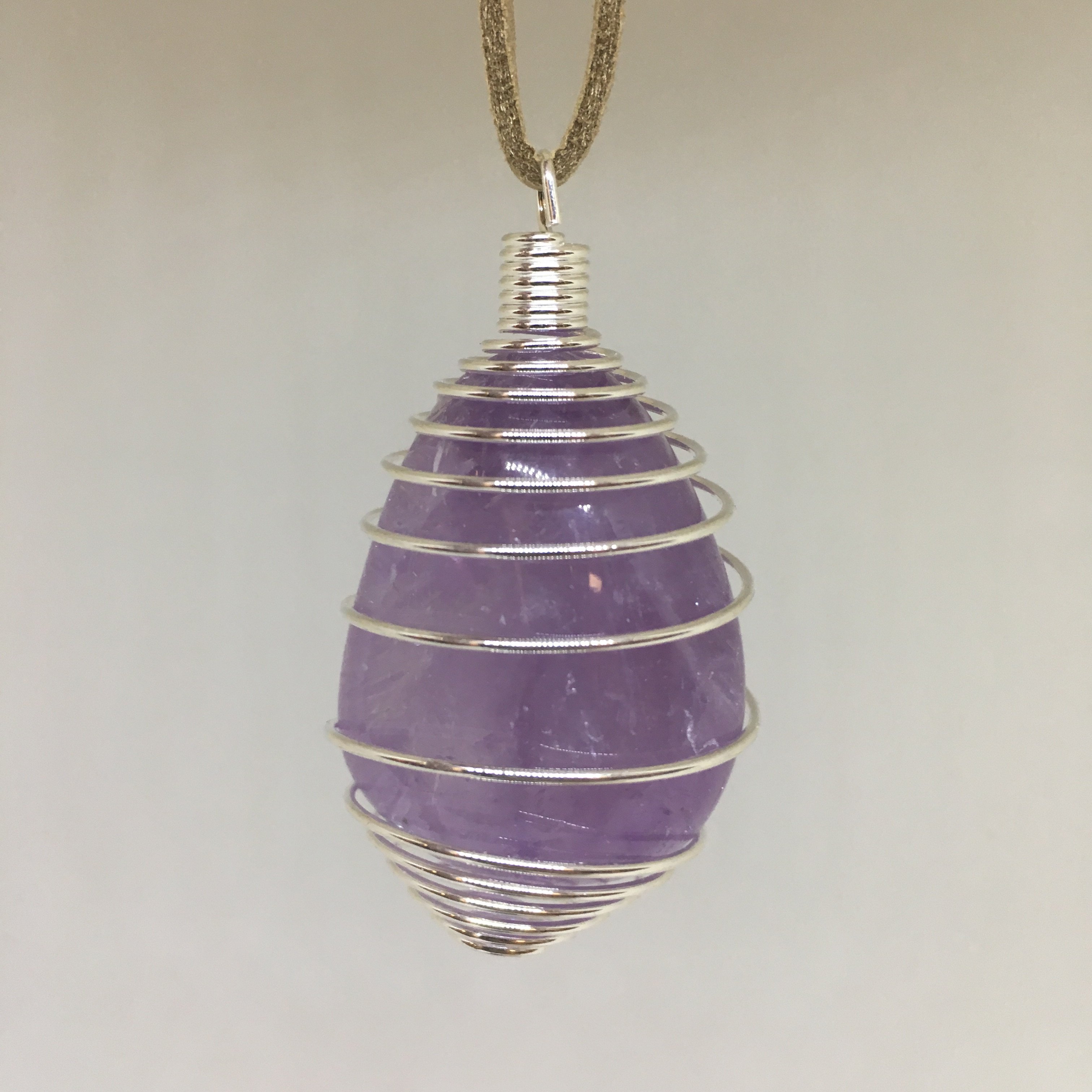 A collection of Tumbled Pendants featuring Opalite, Amethyst, Rose Quartz, Selenite, Angelite, and Hematite, elegantly displayed with a silver cage and tan suede necklace.