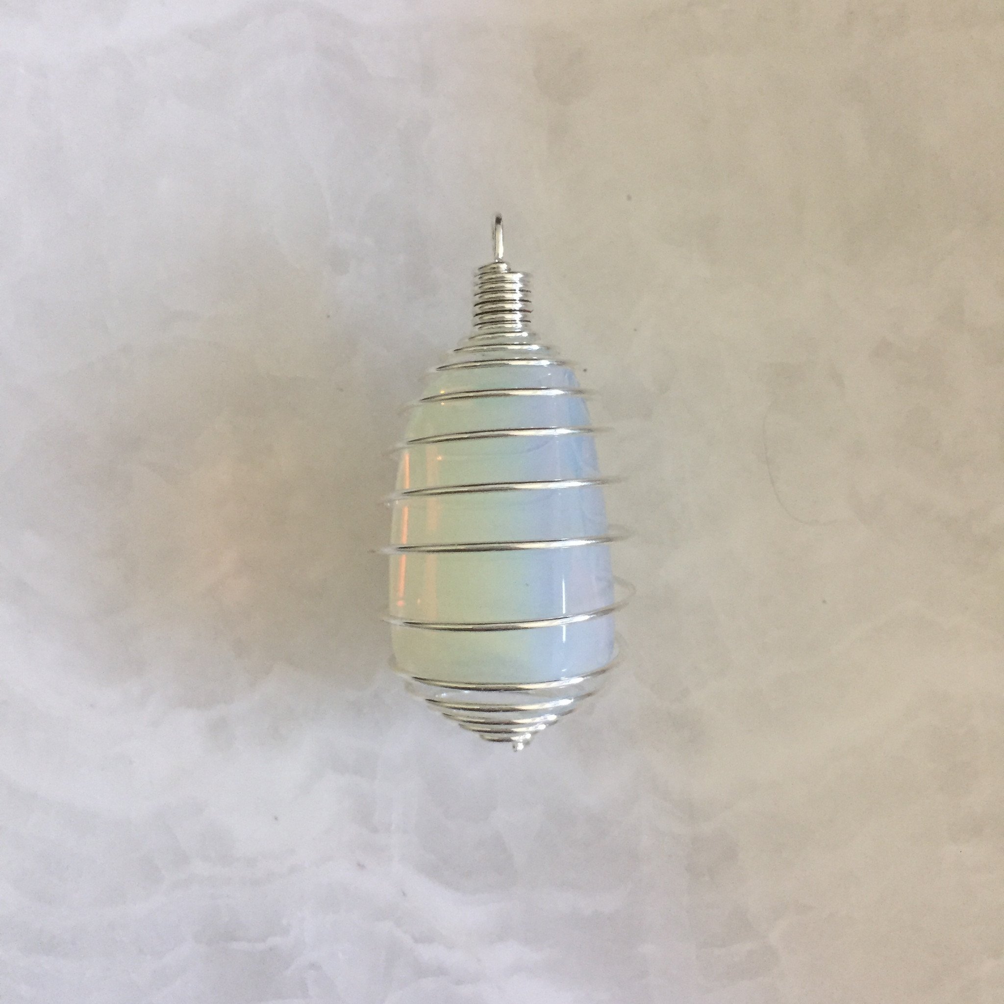 A collection of Tumbled Pendants featuring Opalite, Amethyst, Rose Quartz, Selenite, Angelite, and Hematite, elegantly displayed with a silver cage and tan suede necklace.