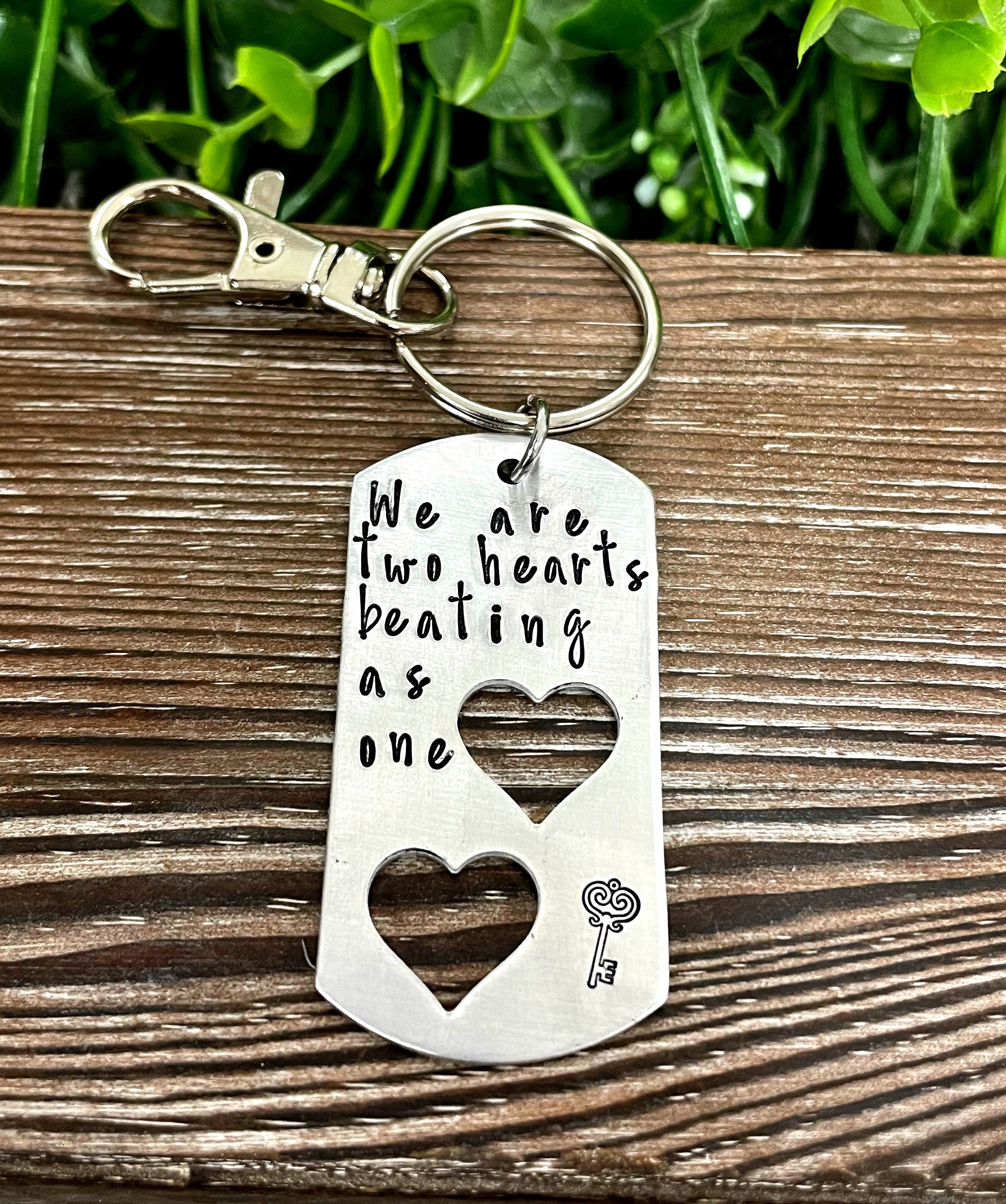 Hand-stamped keychain featuring the phrase 'We are two hearts beating as one', showcasing unique variations in design and craftsmanship.