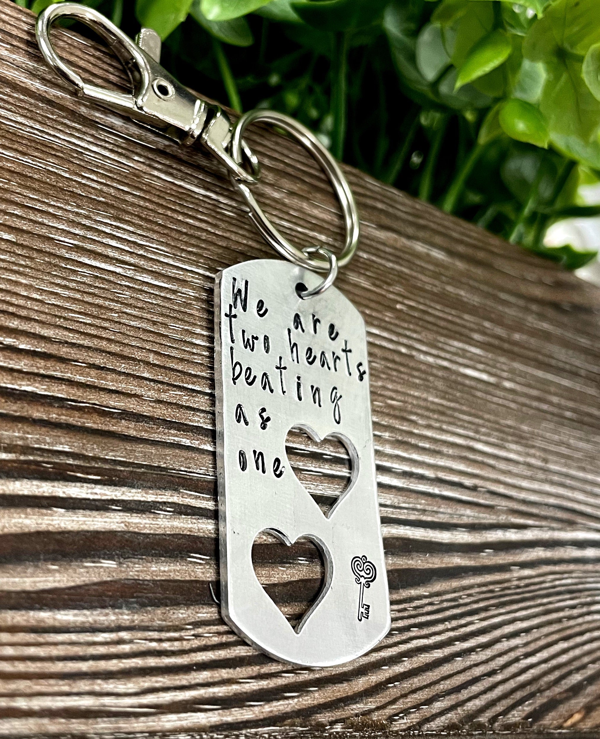 Hand-stamped keychain featuring the phrase 'We are two hearts beating as one', showcasing unique variations in design and craftsmanship.