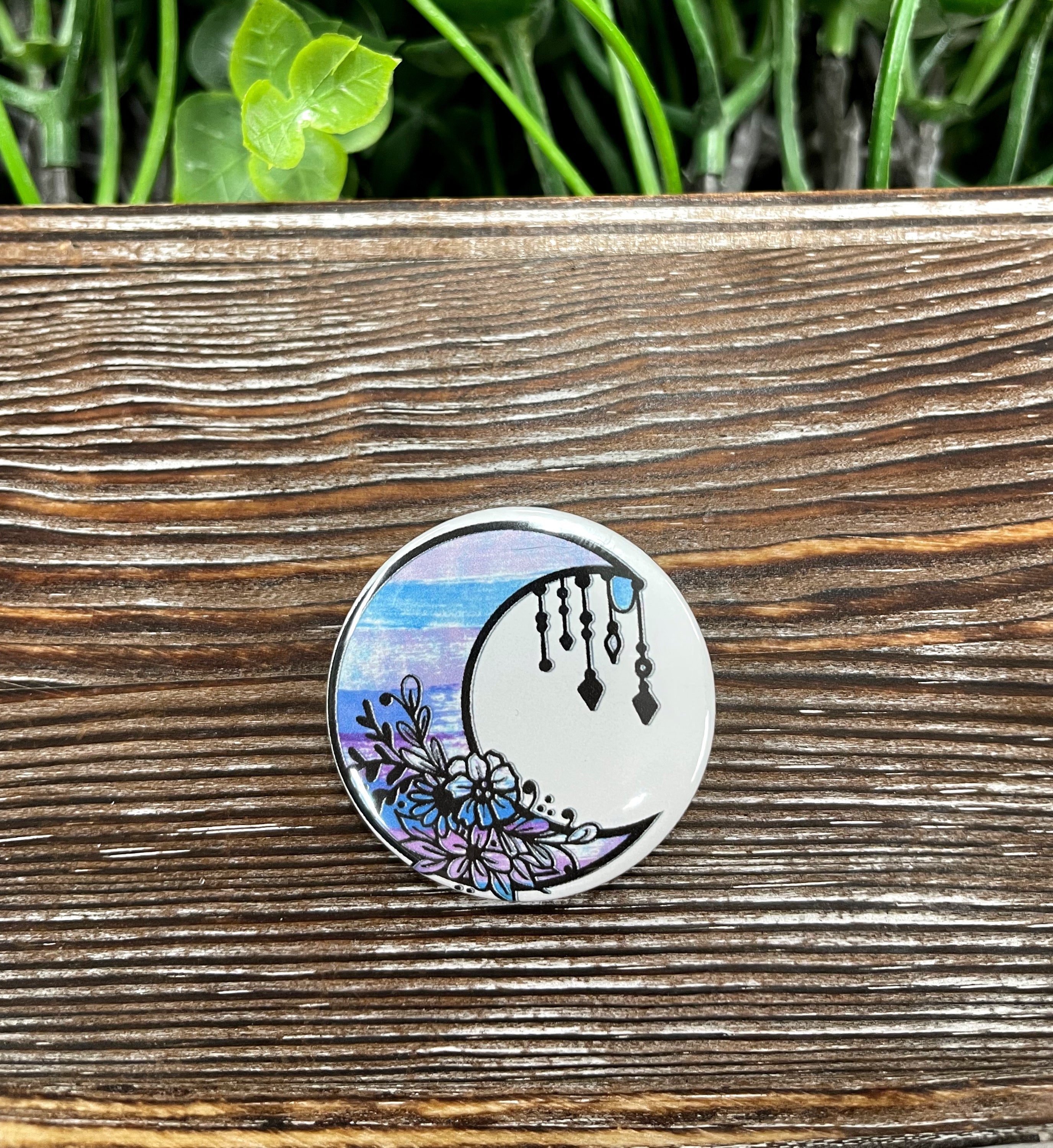 A 1.25-inch button featuring a watercolor crescent moon design, perfect for accessorizing bags and clothing.