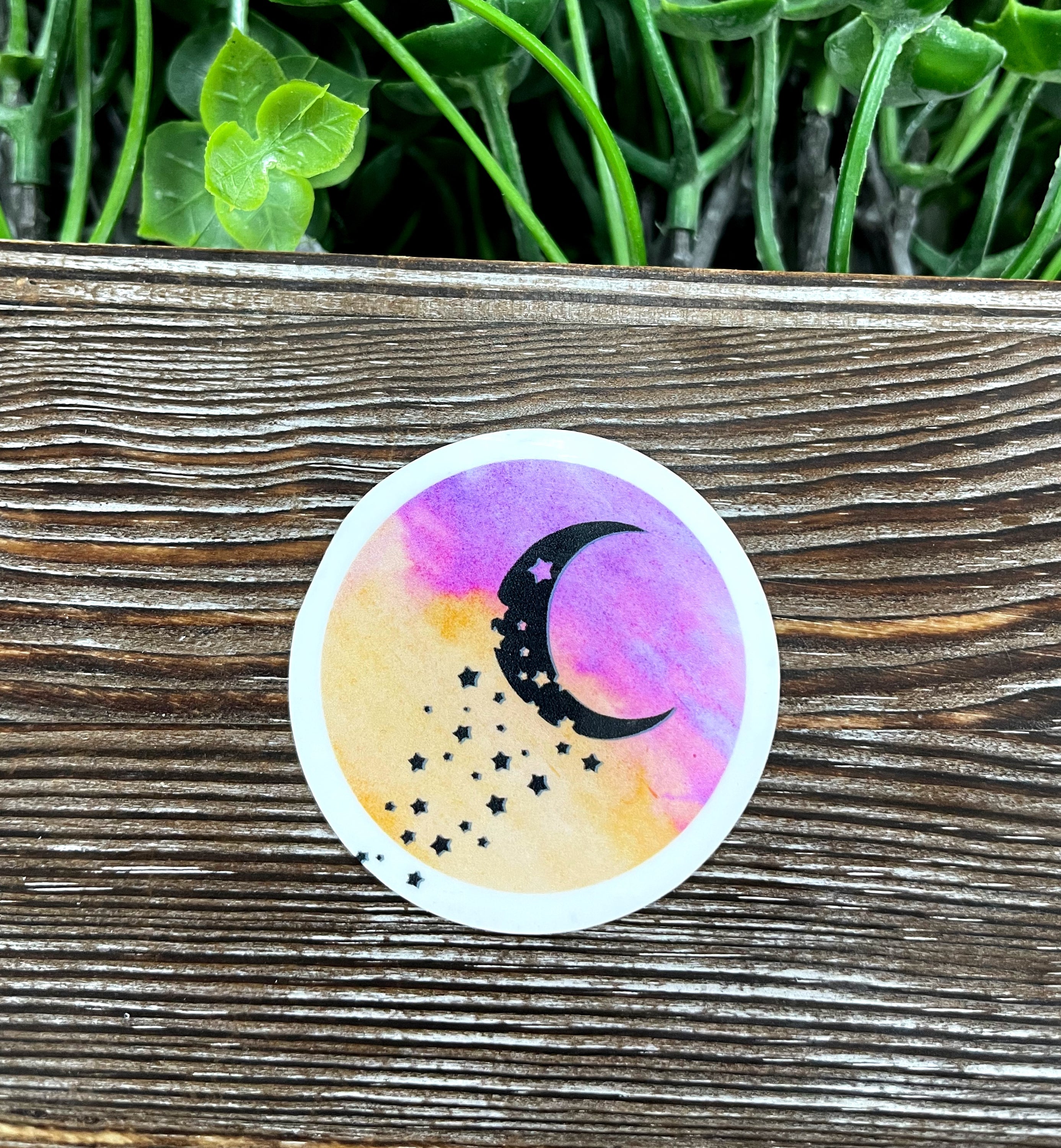 Watercolor Crescent Moon Die Cut Sticker on a smooth surface, showcasing vibrant colors and artistic design.