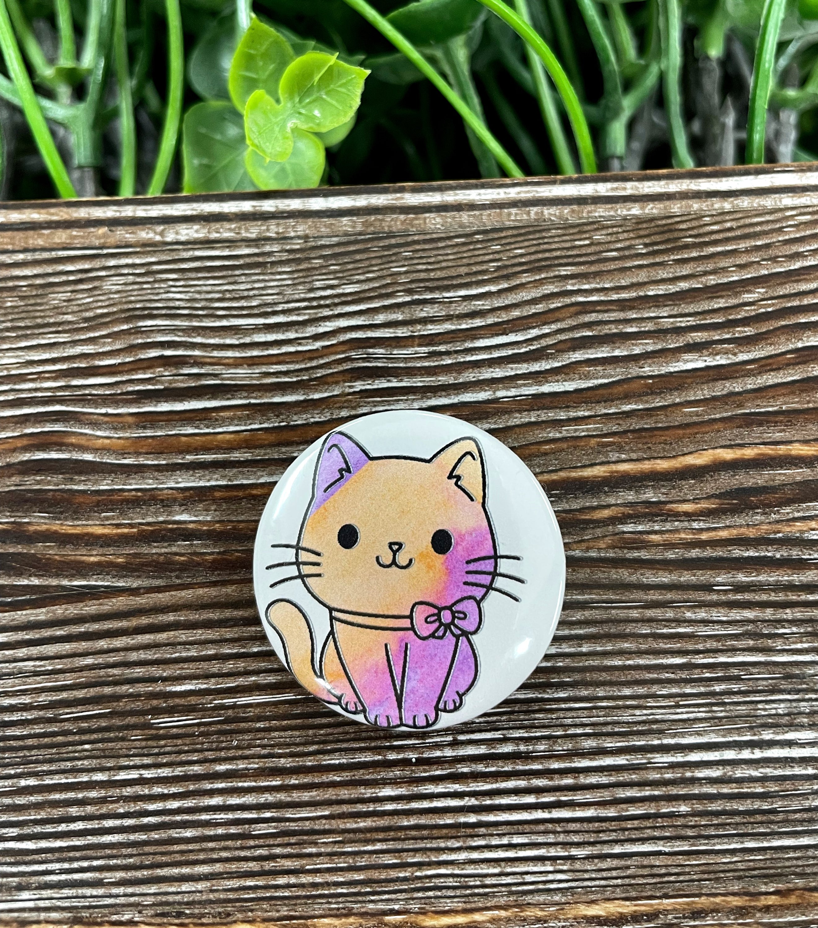 A 1.25-inch button featuring a cute watercolor cat design, perfect for personalizing bags and accessories.