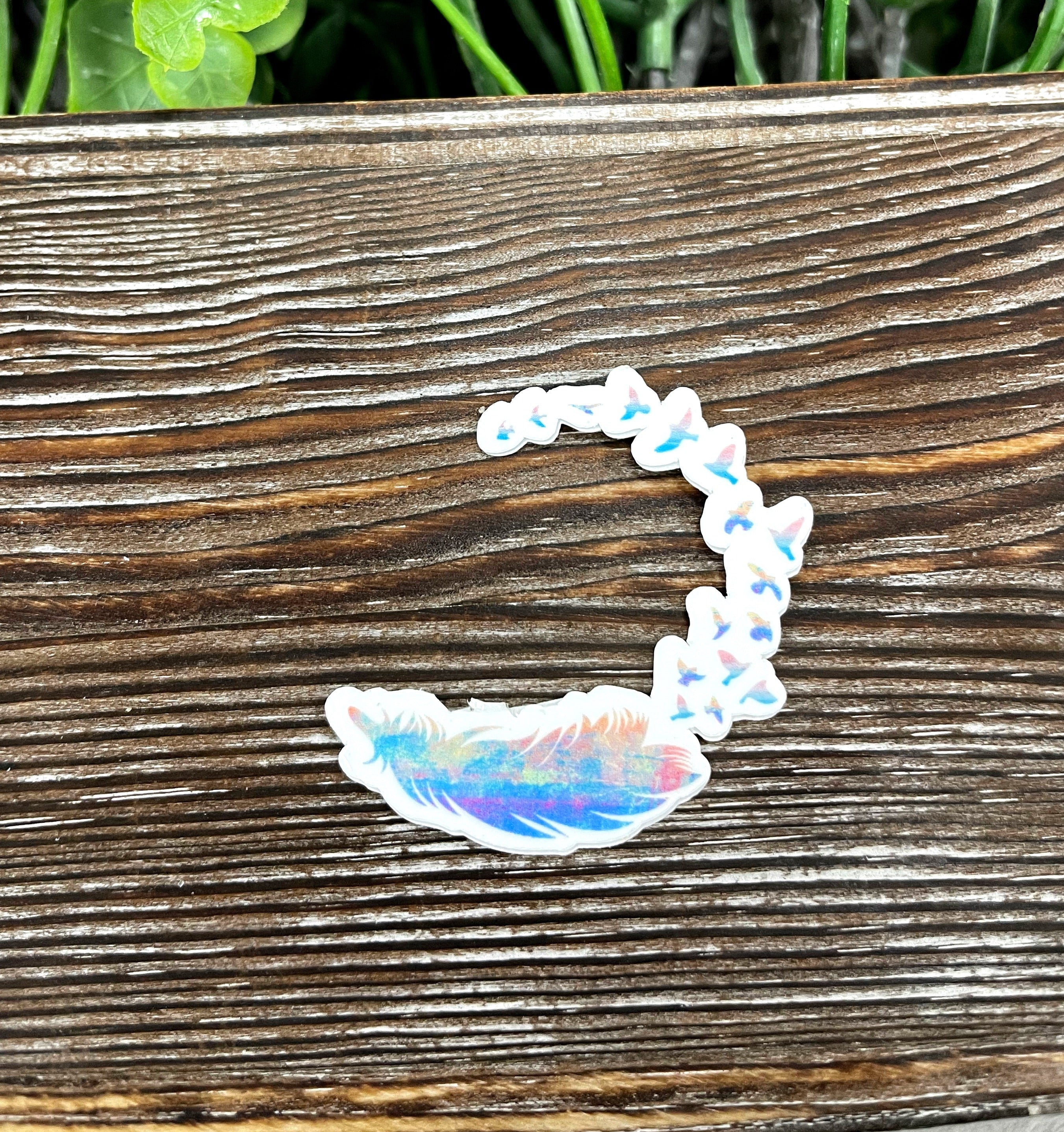 A vibrant watercolor feather die cut sticker transitioning into birds, showcasing artistic design on a smooth surface.