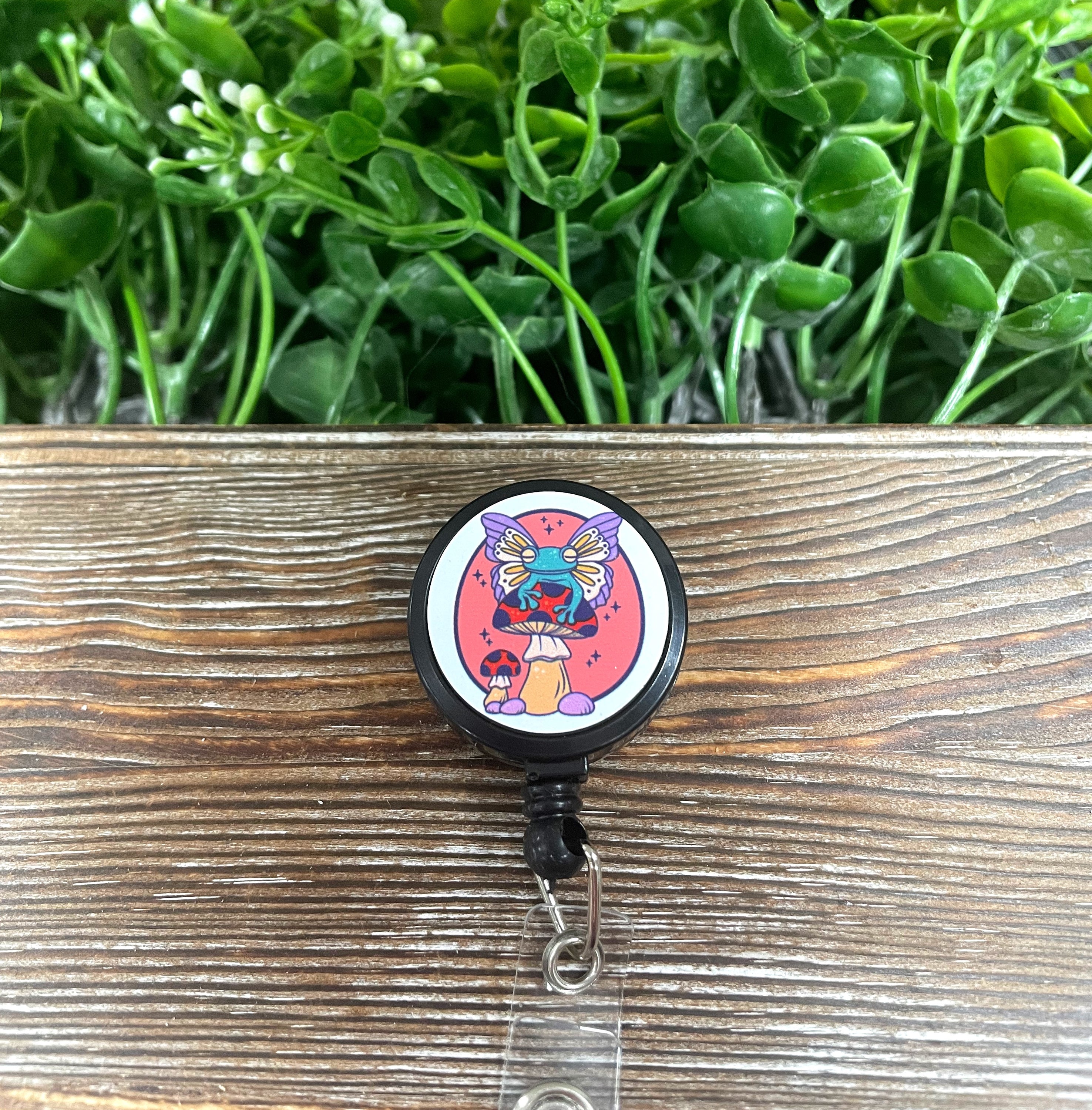 A colorful retractable badge reel featuring a whimsical winged toad sitting on a toadstool, showcasing a boho style.