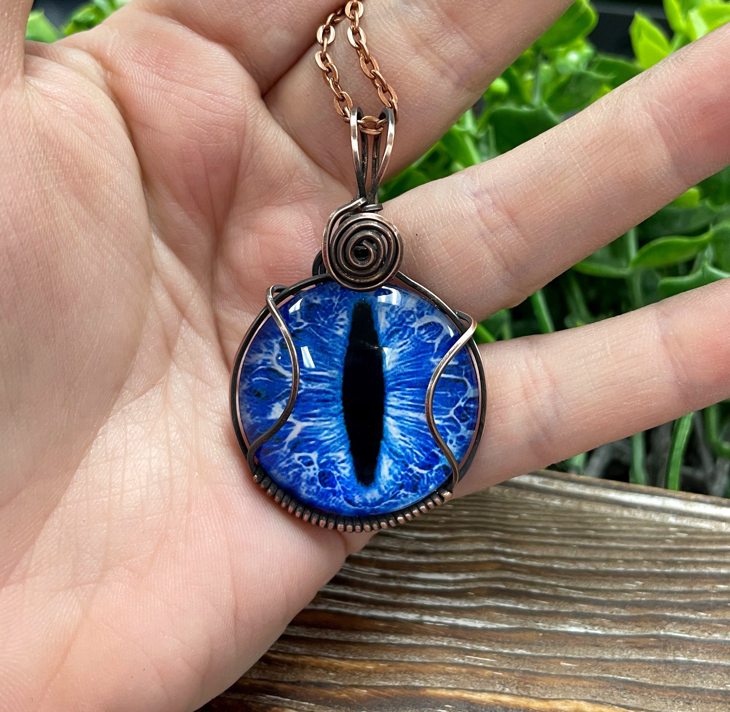 Wire Wrapped Blue Dragon Eye Glass Cabochon Pendant featuring a blue dragon eye design wrapped in oxidized copper wire on a 21-inch cord.