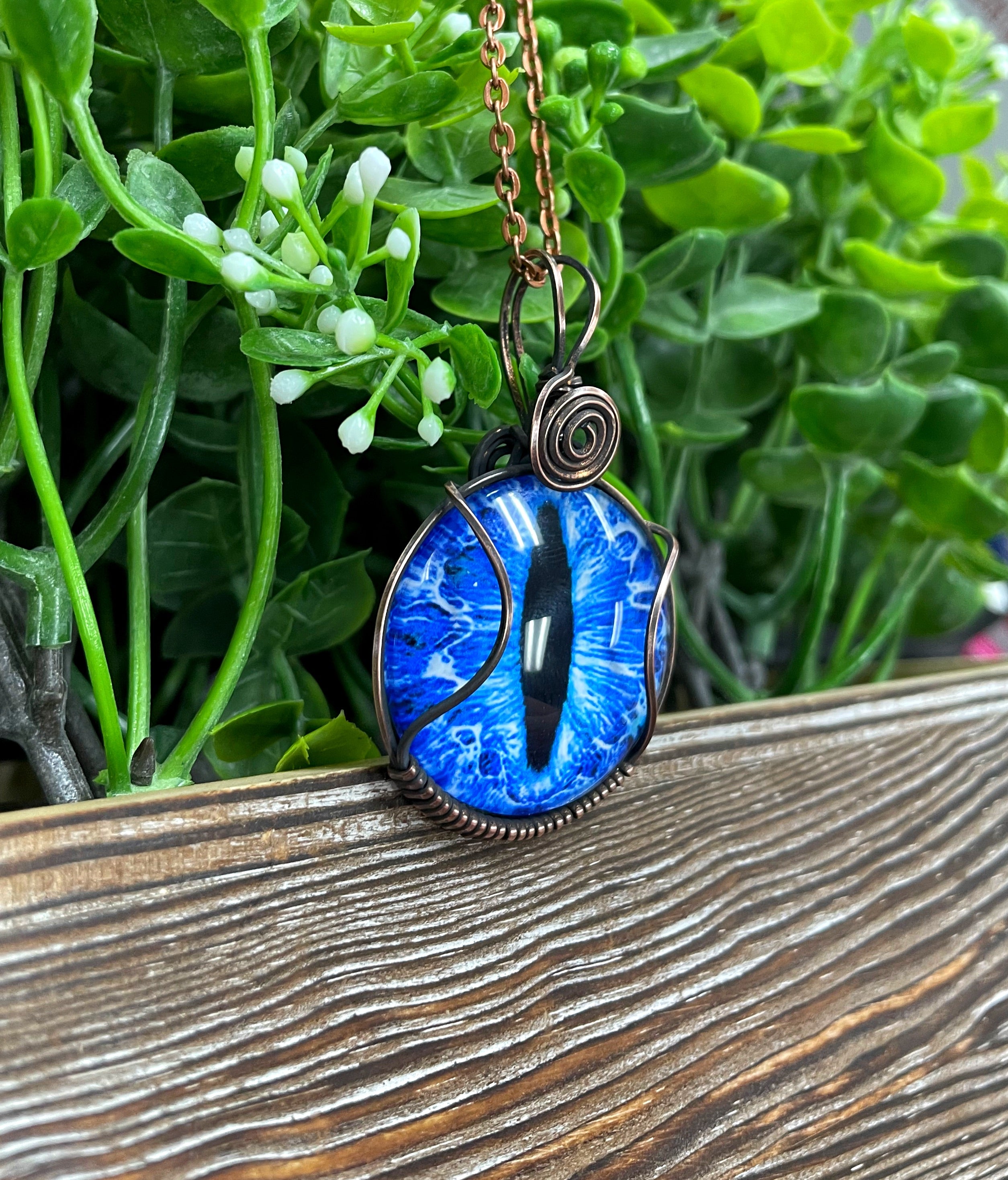 Wire Wrapped Blue Dragon Eye Glass Cabochon Pendant featuring a blue dragon eye design wrapped in oxidized copper wire on a 21-inch cord.