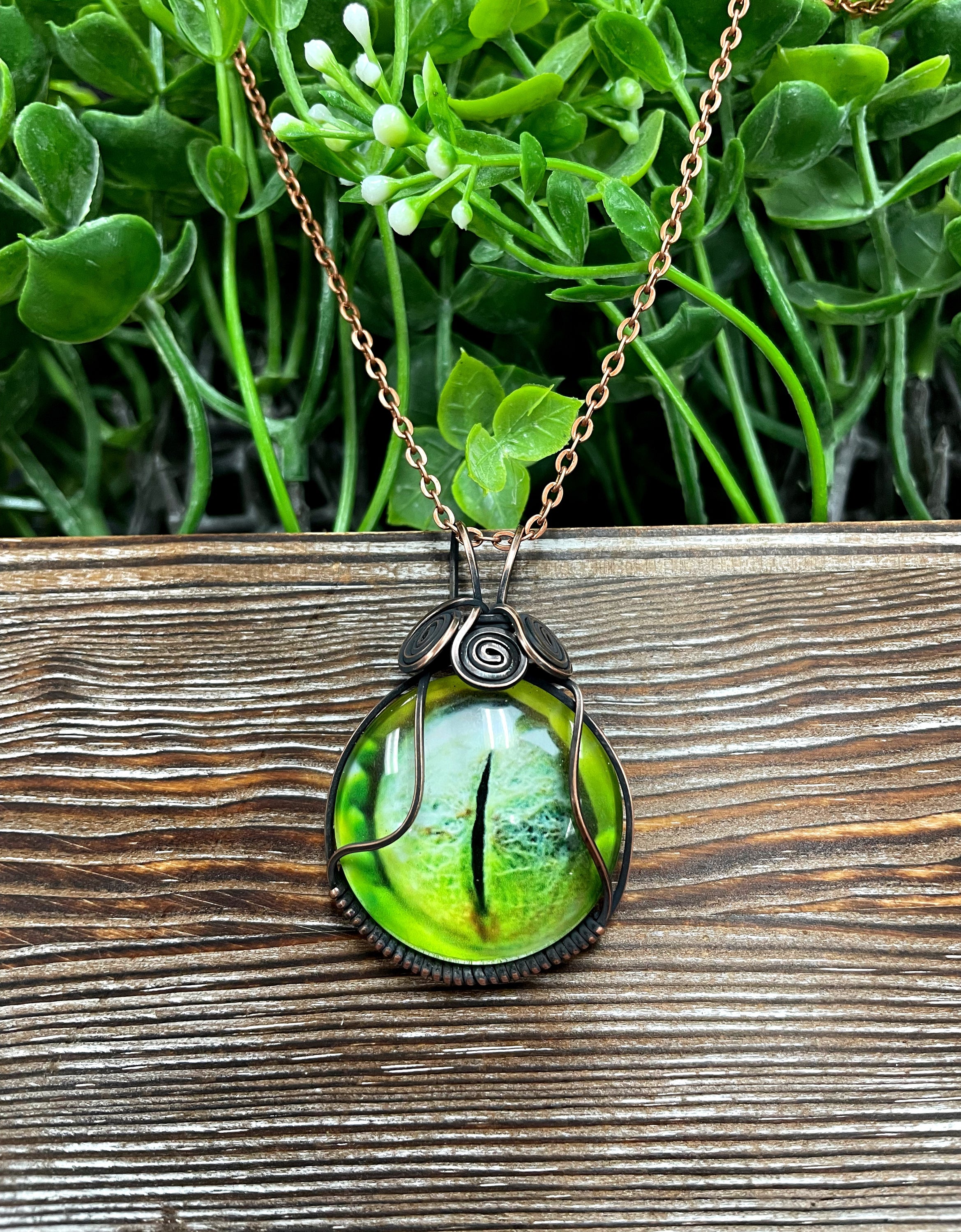 Wire Wrapped Green Reptile Eye Glass Cabochon Pendant featuring a reptile eye design wrapped in oxidized copper wire on a 21-inch cord.