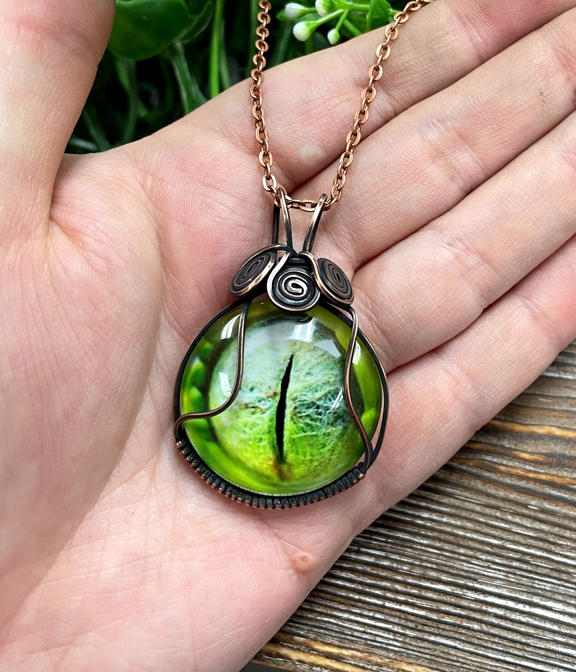 Wire Wrapped Green Reptile Eye Glass Cabochon Pendant featuring a reptile eye design wrapped in oxidized copper wire on a 21-inch cord.