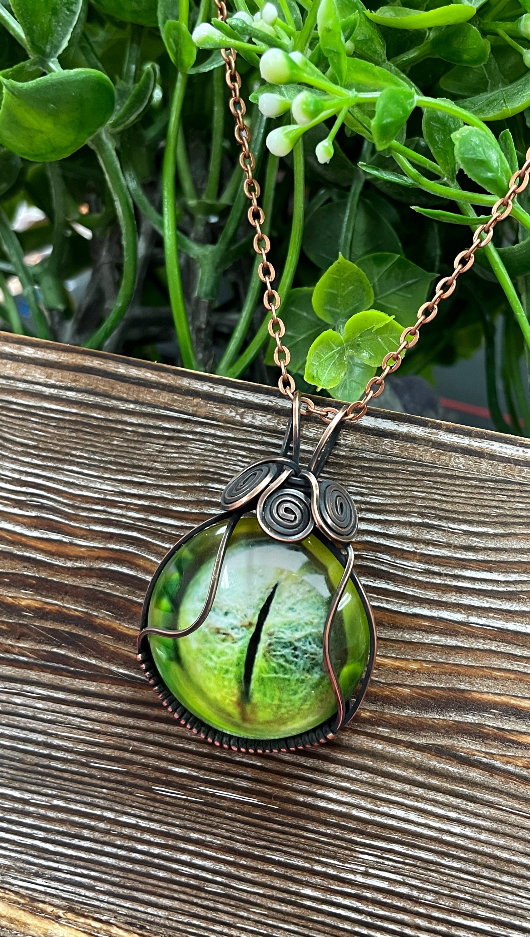 Wire Wrapped Green Reptile Eye Glass Cabochon Pendant featuring a reptile eye design wrapped in oxidized copper wire on a 21-inch cord.