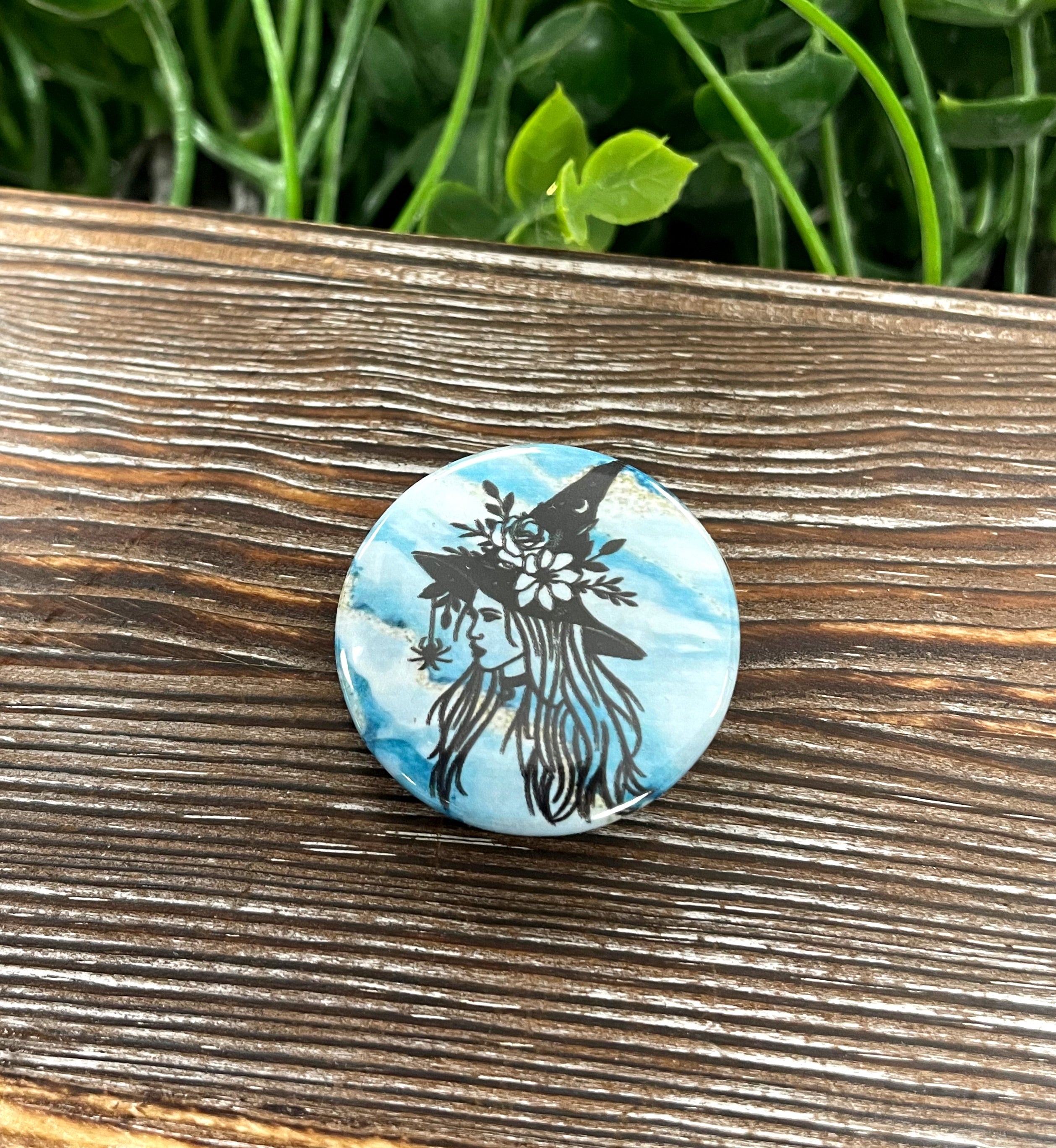 Witch silhouette graphic art button with blue and white marbling design, measuring 1.25 inches in diameter.