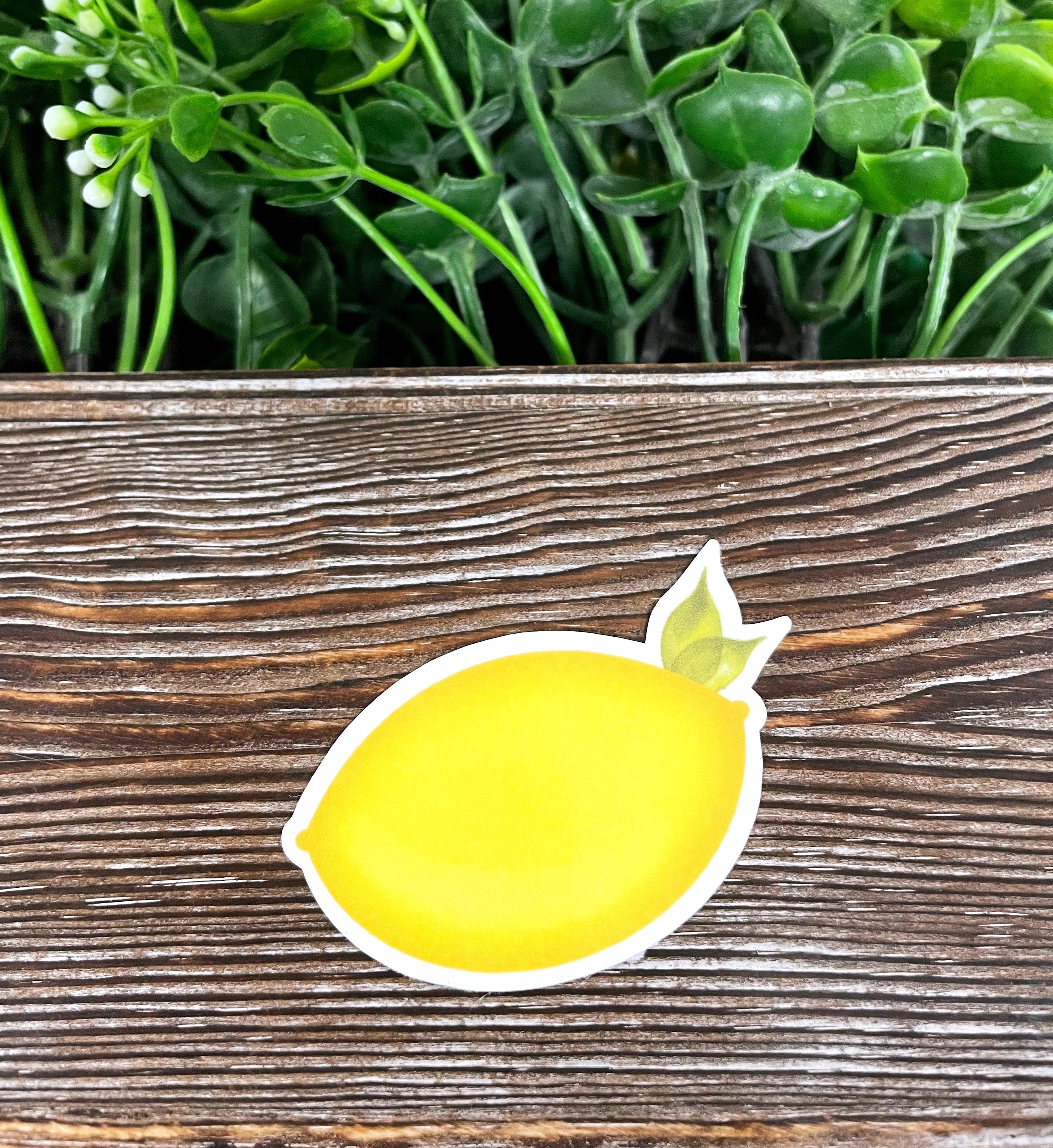 A vibrant yellow lemon die cut sticker on a smooth surface, showcasing its bright color and graphic art design.