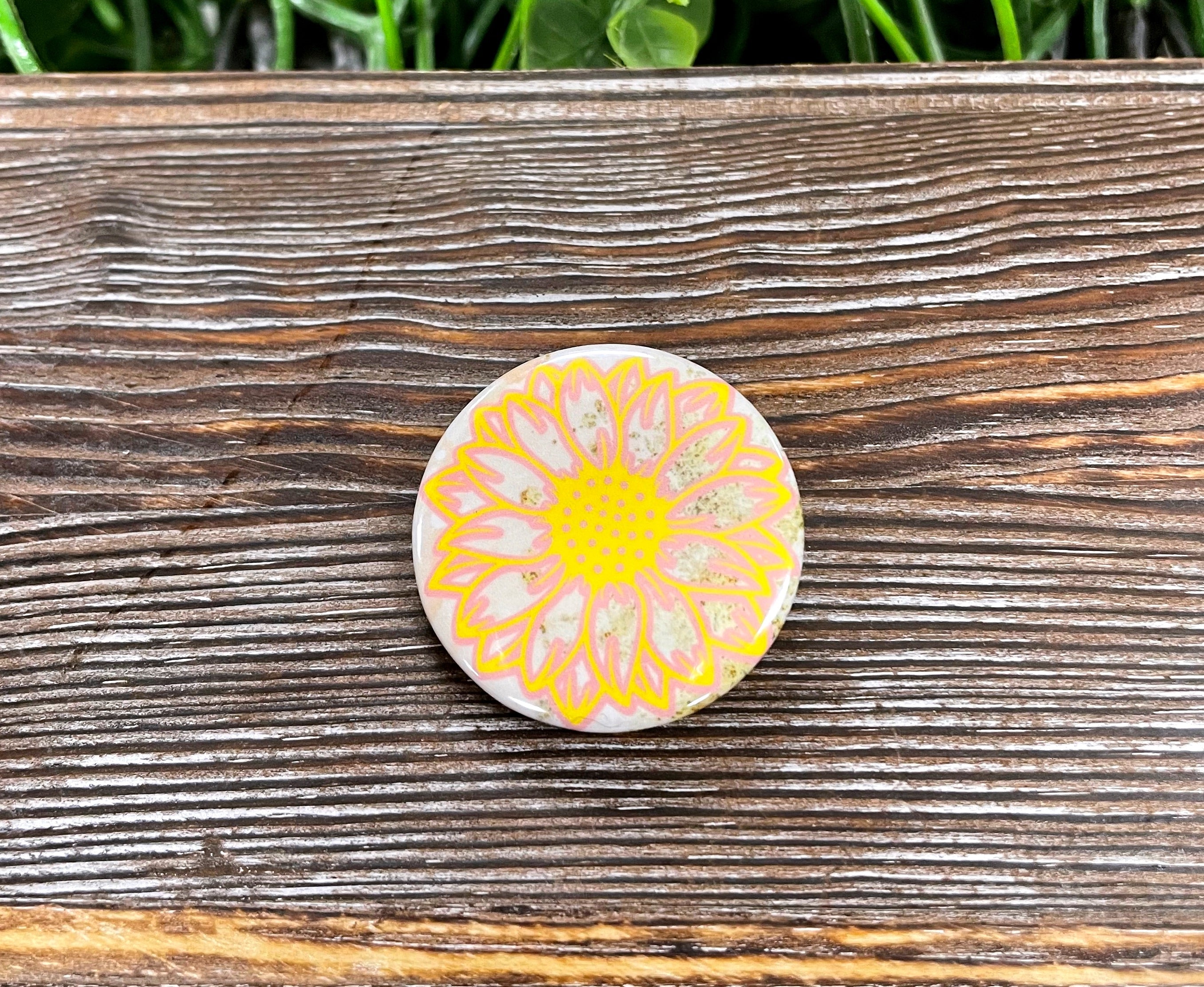 A vibrant 1.25-inch button pin featuring a yellow sunflower graphic design, perfect for personalizing bags and accessories.