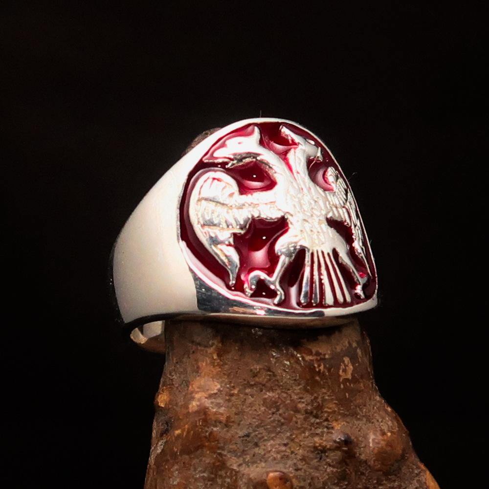 A beautifully crafted sterling silver men's ring featuring a twin head eagle design with red enamel detailing, showcasing its intricate craftsmanship.