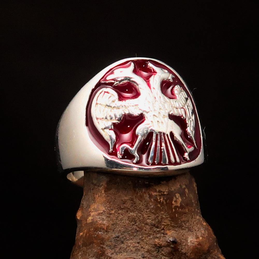 A beautifully crafted sterling silver men's ring featuring a twin head eagle design with red enamel detailing, showcasing its intricate craftsmanship.